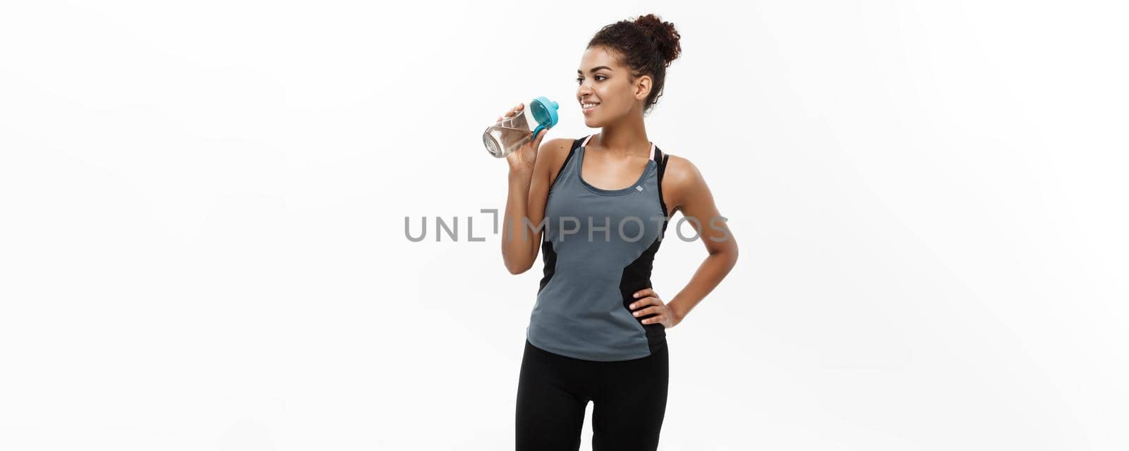 Healthy and Fitness concept - beautiful African American girl in sport clothes drinking water after workout. Isolated on white studio background.