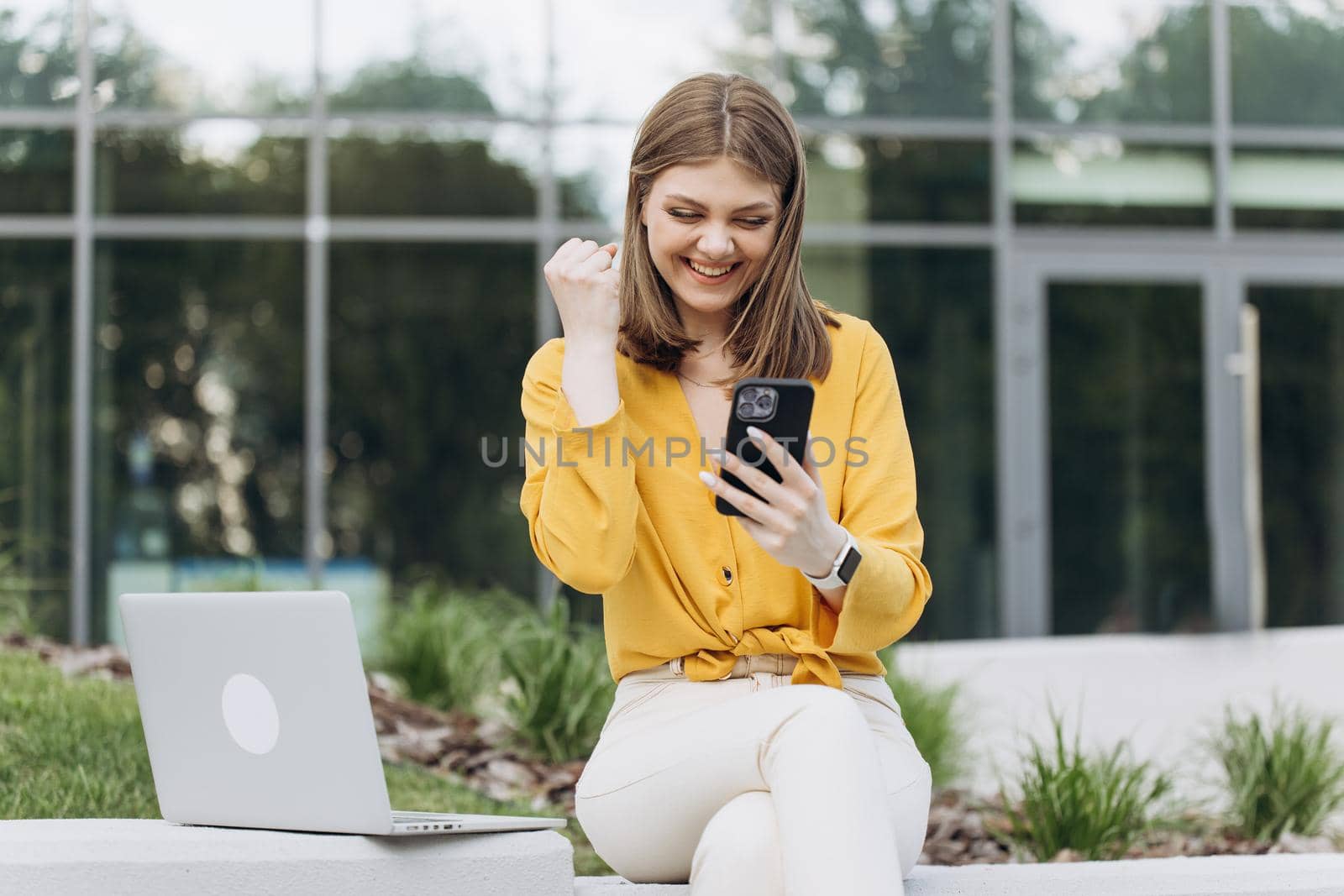Surprised lady celebrating victory on smartphone outdoor. Portrait of happy business caucasian woman enjoy success on mobile phone. Joyful girl reading good news on phone by uflypro