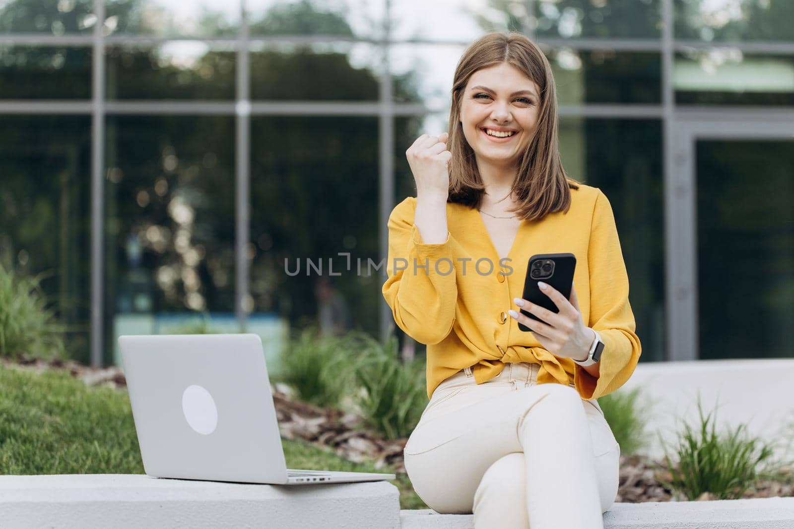 Joyful girl reading good news on phone. Surprised lady celebrating victory on smartphone outdoor. Portrait of happy business caucasian woman enjoy success on mobile phone by uflypro