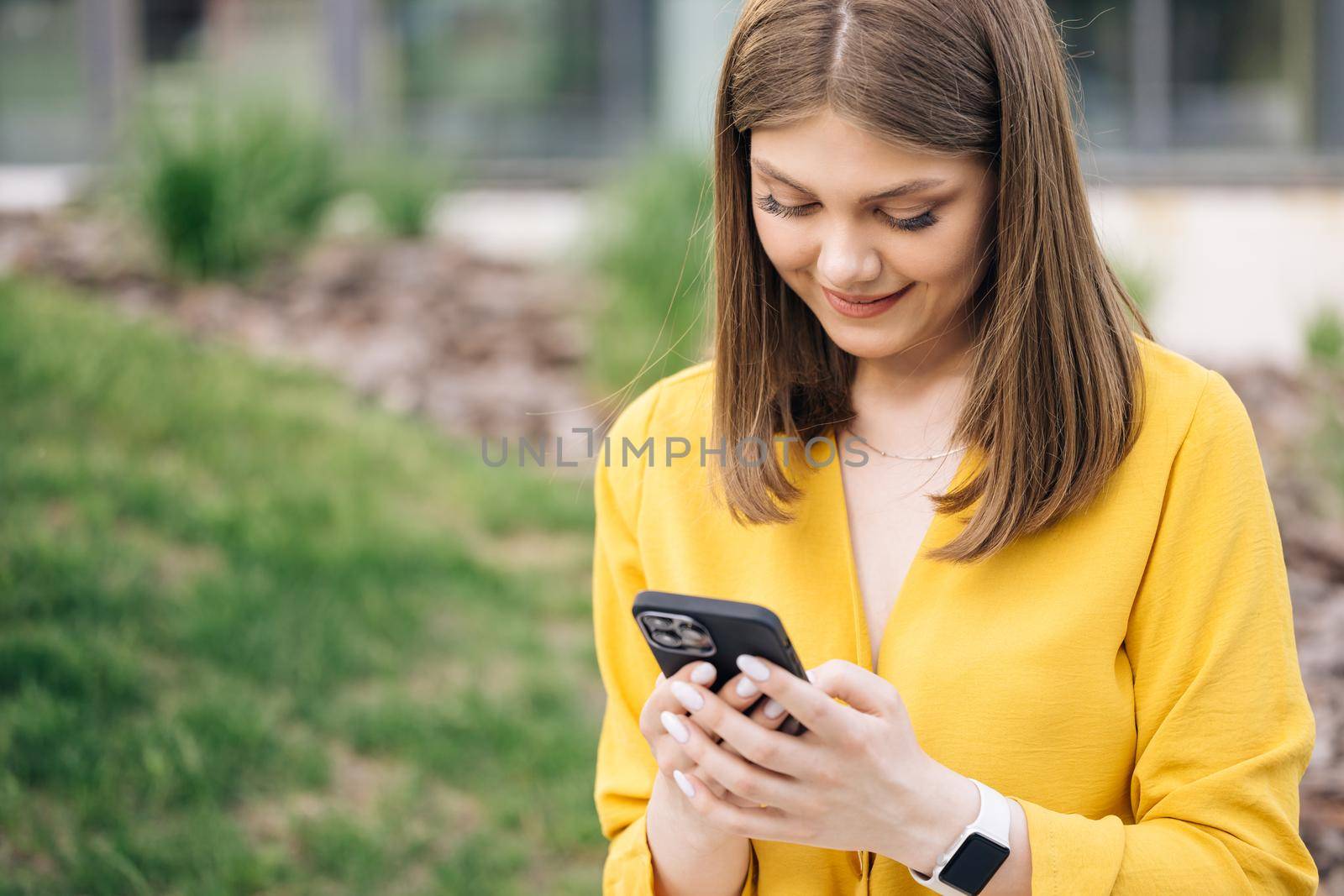 Portrait of business woman reading messages on cellphone. Happy businesswoman using mobile phone at remote workplace. Smiling woman browsing internet on smartphone near office.