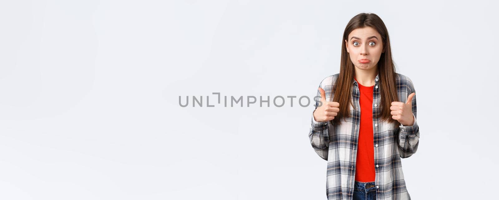 Lifestyle, different emotions, leisure activities concept. Not bad I guess. Cute girl surprised with positive result, show thumb-up and make confused expression, standing white background by Benzoix