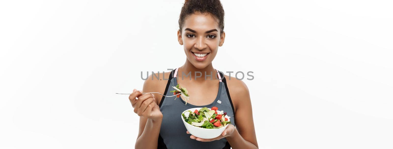 Healthy and Fitness concept - Beautiful American African lady in fitness clothes on diet eating fresh salad. Isolated on white background