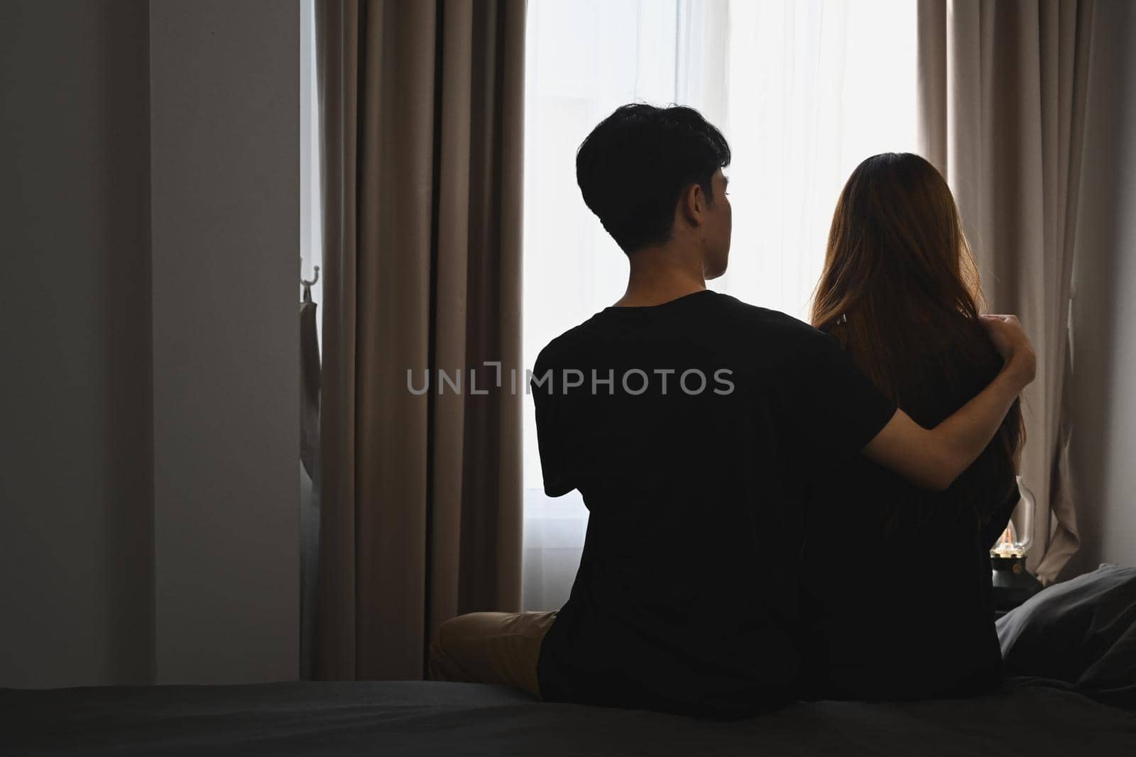 Back view of young man embracing his wife and sitting in bed room. Comforting, encouraging and understanding. by prathanchorruangsak