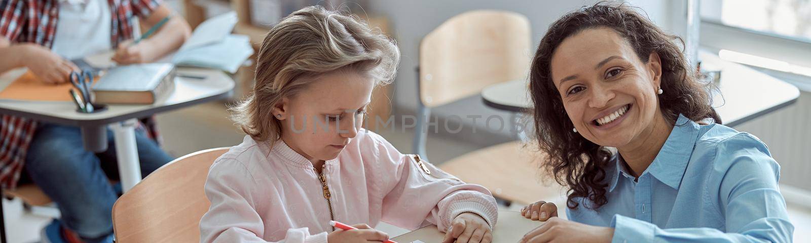 Happy kind teacher is helping kids in elementary school lessons.