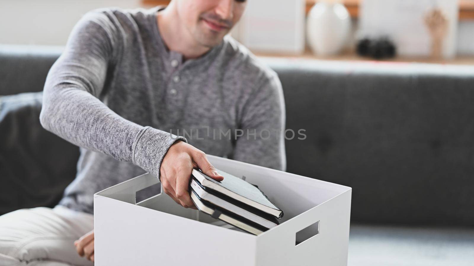 Happy man sitting on couch preparing personal stuff for moving into new house.