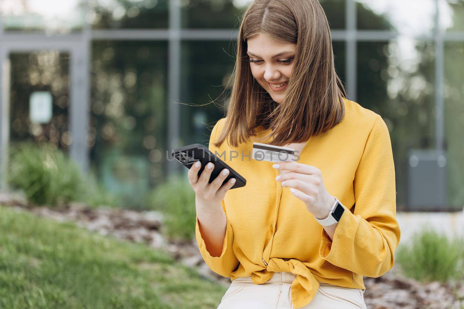 Smartphone communication technology banking money finance browsing paying. Woman is entering credit card number for online shopping using mobile phone sitting at urban city buildings outdoor by uflypro