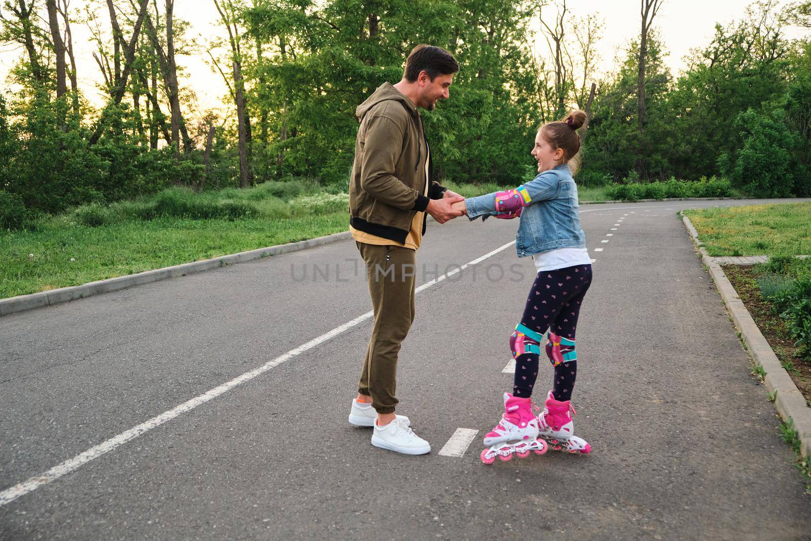 Father teaching his daughter to skate on roller skates. Happy kid learning skating. Family spending time together. Sunny summer day on suburb street