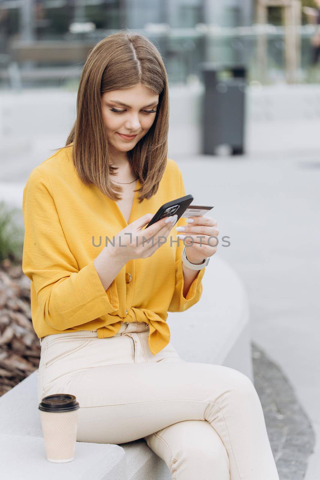 Vertical shot of young white caucasian woman holding credit card using a digital mobile device and buying online, internet shopping. Female hand typing bank card number into a smartphone.