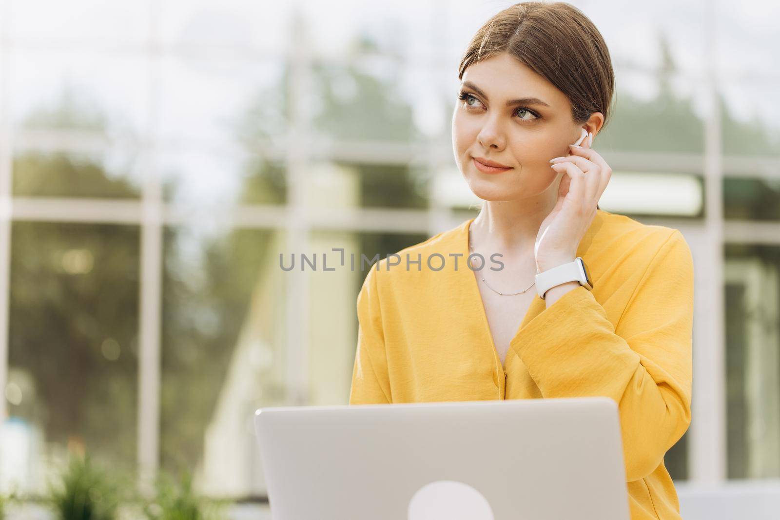 Portrait of beautiful young caucasian woman listening to favorite music in wireless headphones while sitting on bench using laptop computer. Happy european girl enjoying break time and soft dance by uflypro