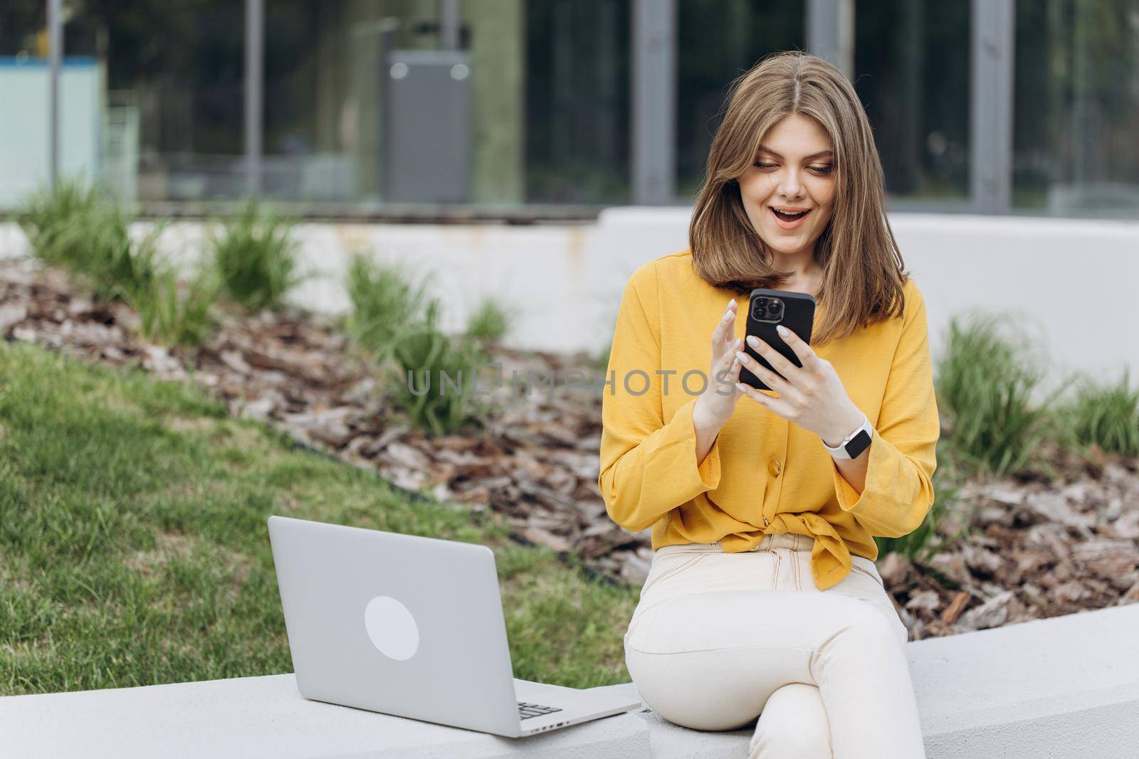 Portrait of happy business caucasian woman enjoy success on mobile phone. Closeup joyful girl reading good news on phone. Surprised lady celebrating victory on smartphone outdoor by uflypro