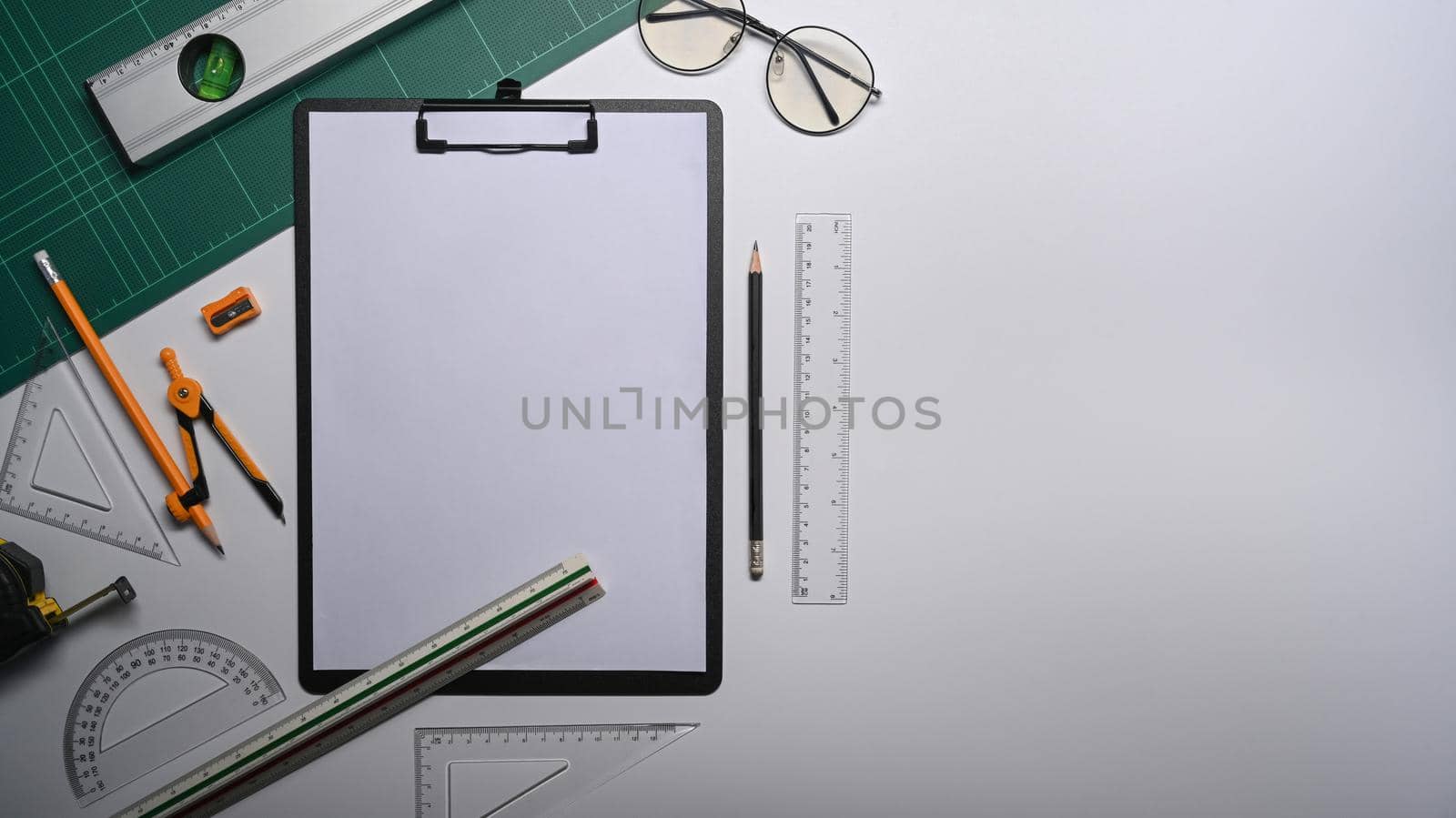 Top view clipboard, tape measure and stationery on white table.