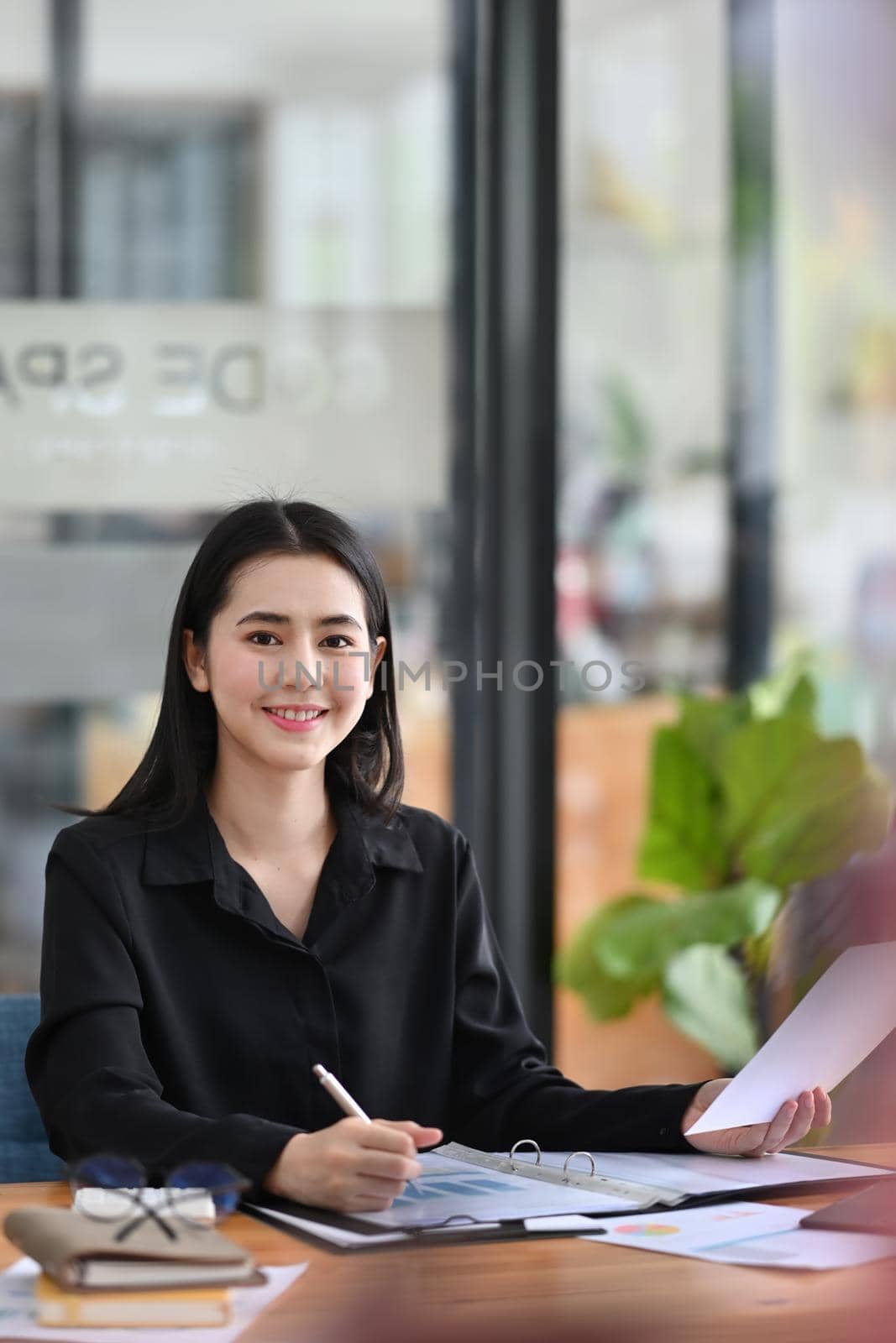 Portrait of attractive businesswoman sitting at her office desk and smiling to camera. by prathanchorruangsak
