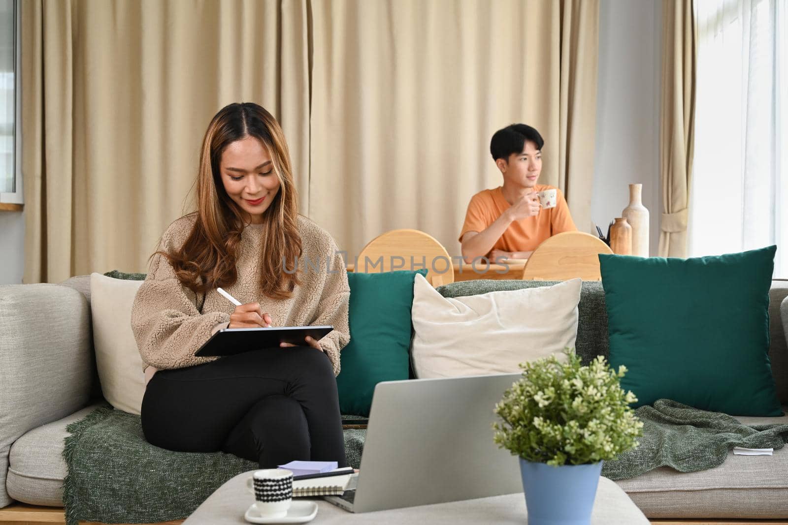 Cheerful asian woman sitting in living room with her husband and using digital tablet.
