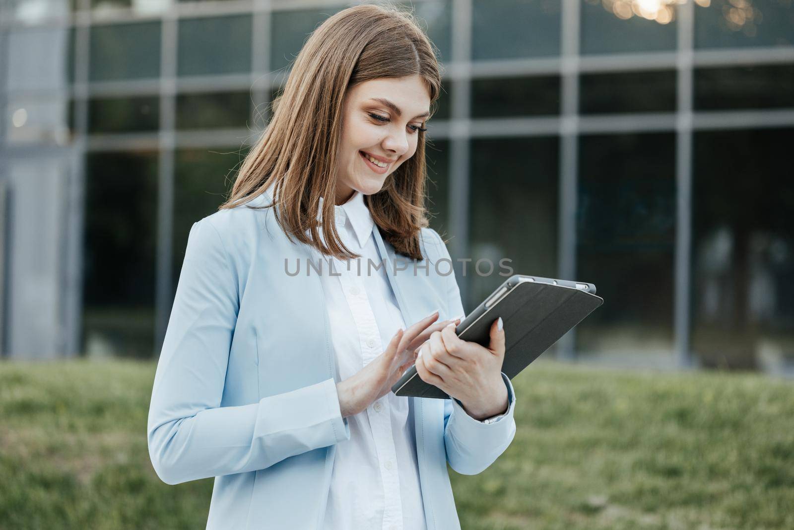 Beautiful young woman engaged in business using tablet computer reading financial news online. European hairstyle. Corporate people by uflypro
