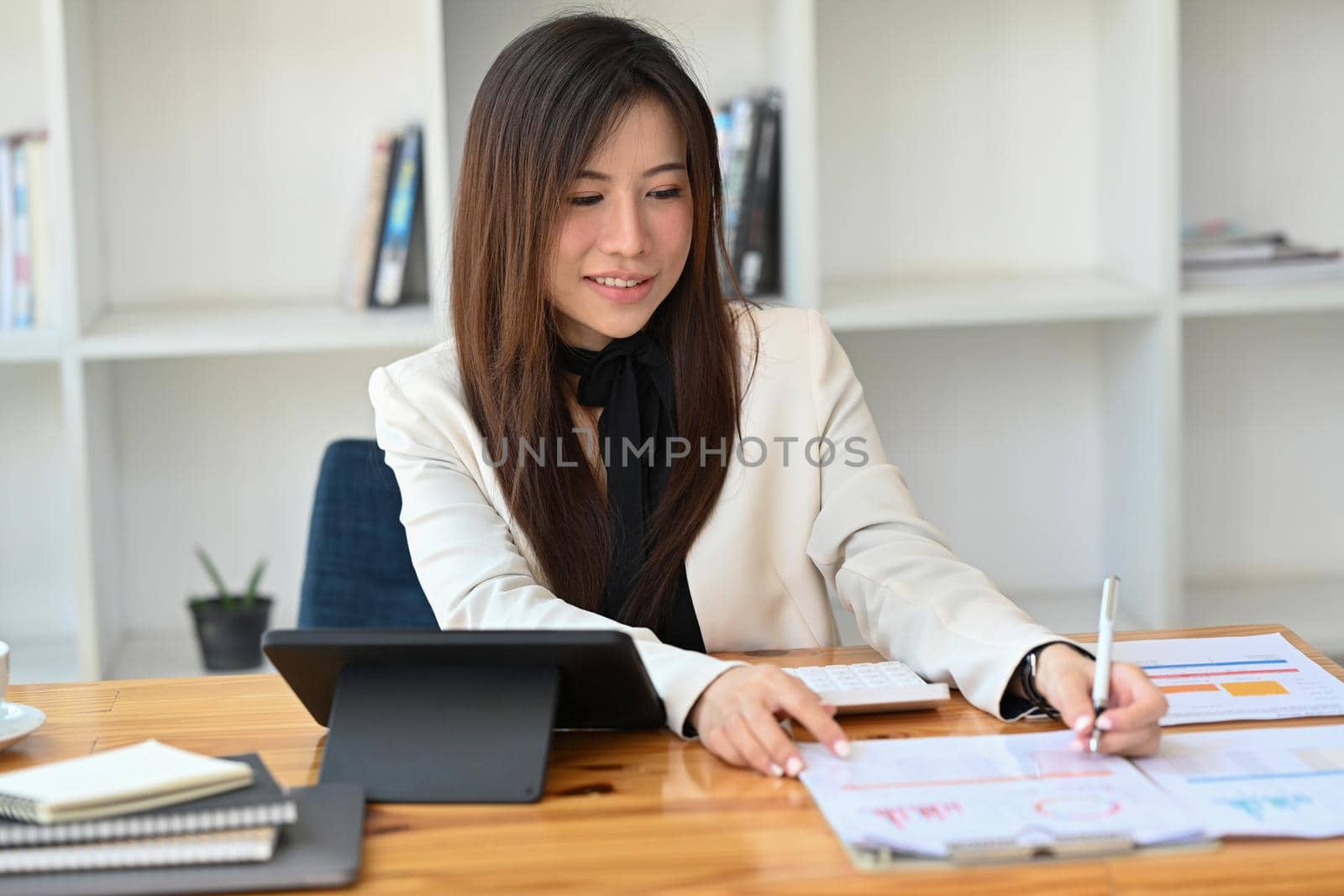 Charming businesswoman checking financial reports at office desk.