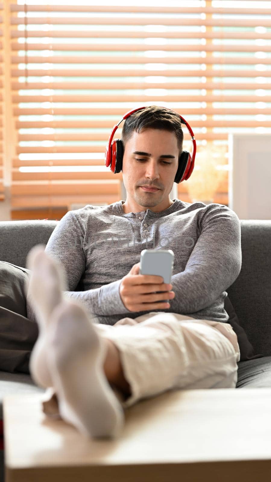 Portrait young man in casual clothes with headphone using mobile phone on sofa. by prathanchorruangsak