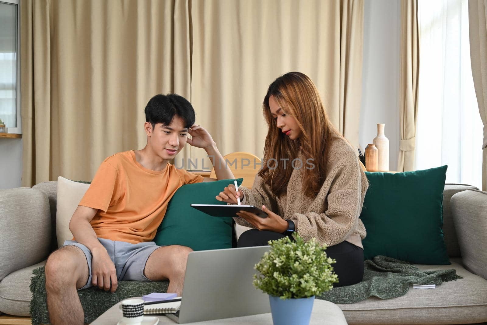 Young asian couple sitting together on couch and surfing internet with digital tablet.