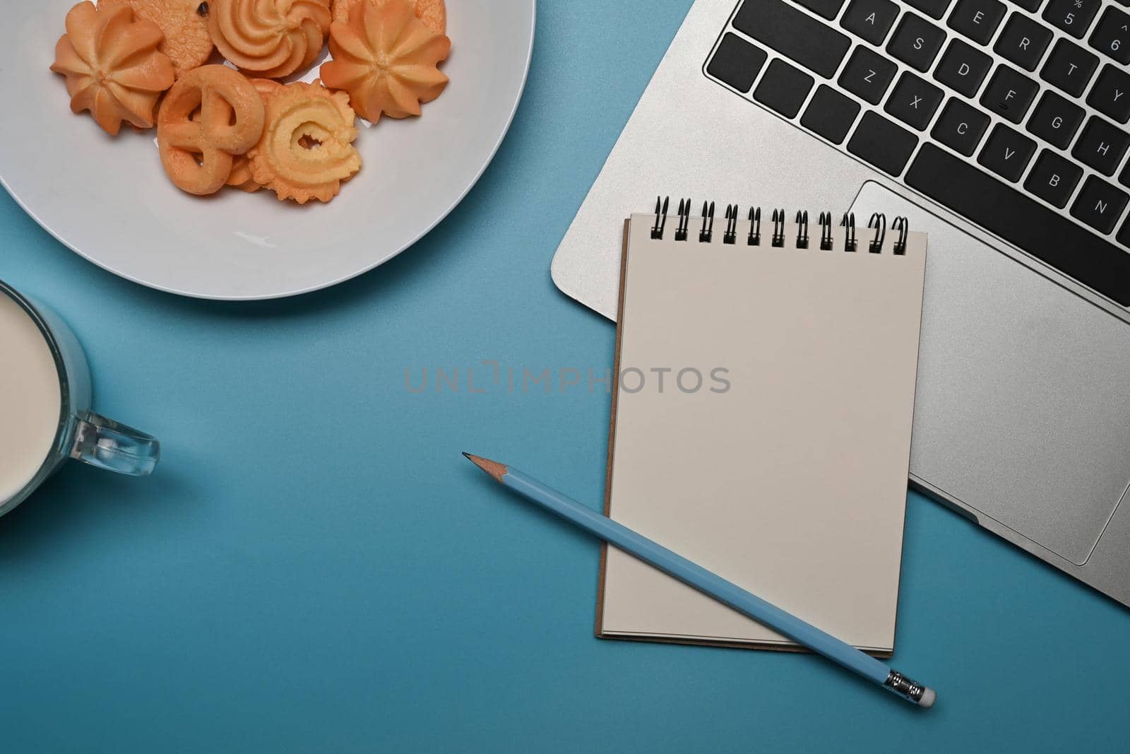 Plate with Danish butter cookies, fresh milk, notebook and laptop on blue background.
