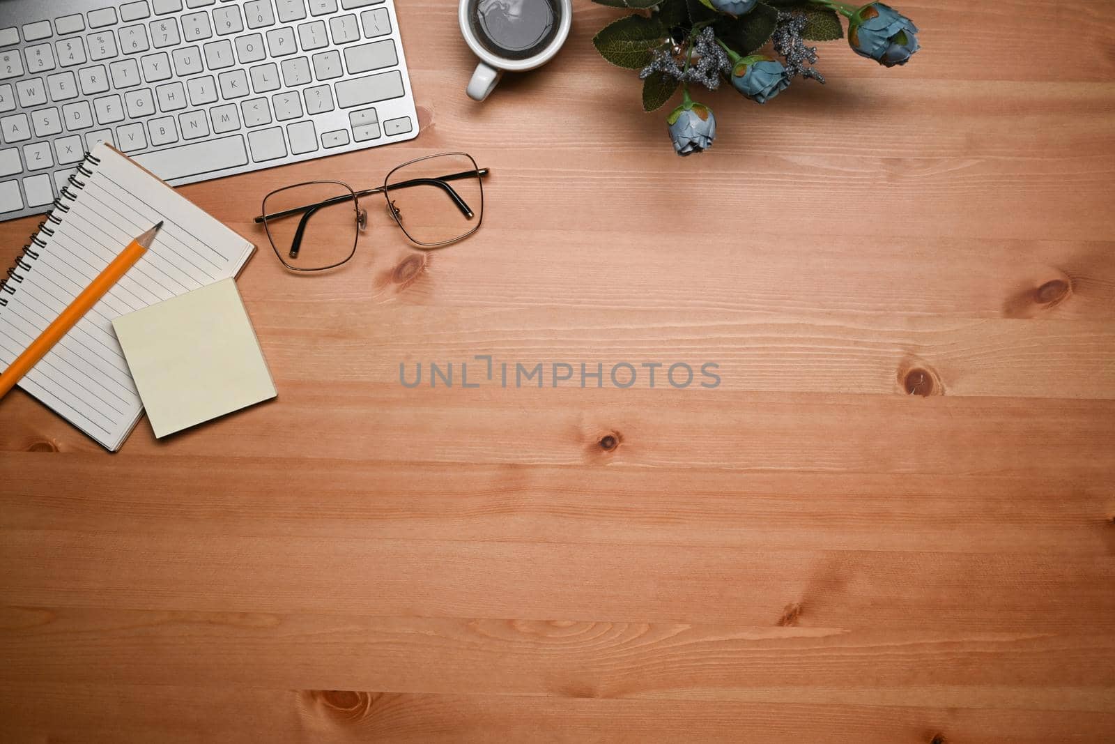 Above view keyboard, glasses, coffee cup and notebook on wooden table. by prathanchorruangsak