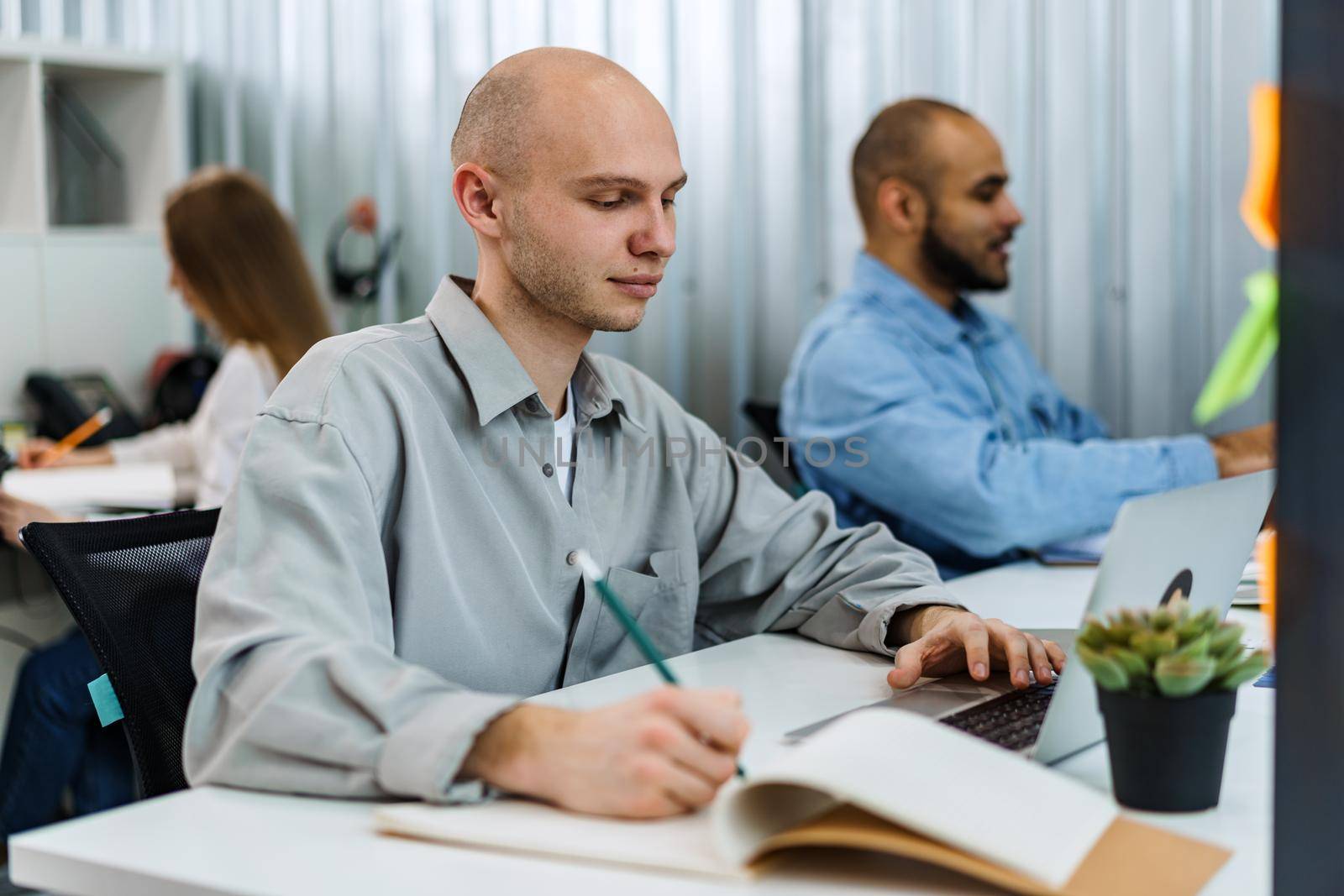 Young bald business man sitting at desk in office, working on computer by Fabrikasimf