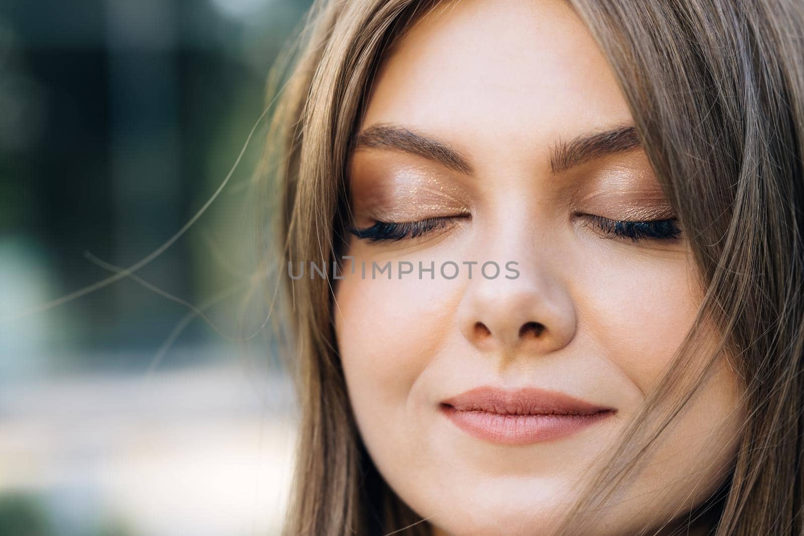 Girl Closing Her Beautiful Blue Eyes Wind Blowing on Brunette Hair. Close up of Woman's Face. Natural Beauty Face Female.
