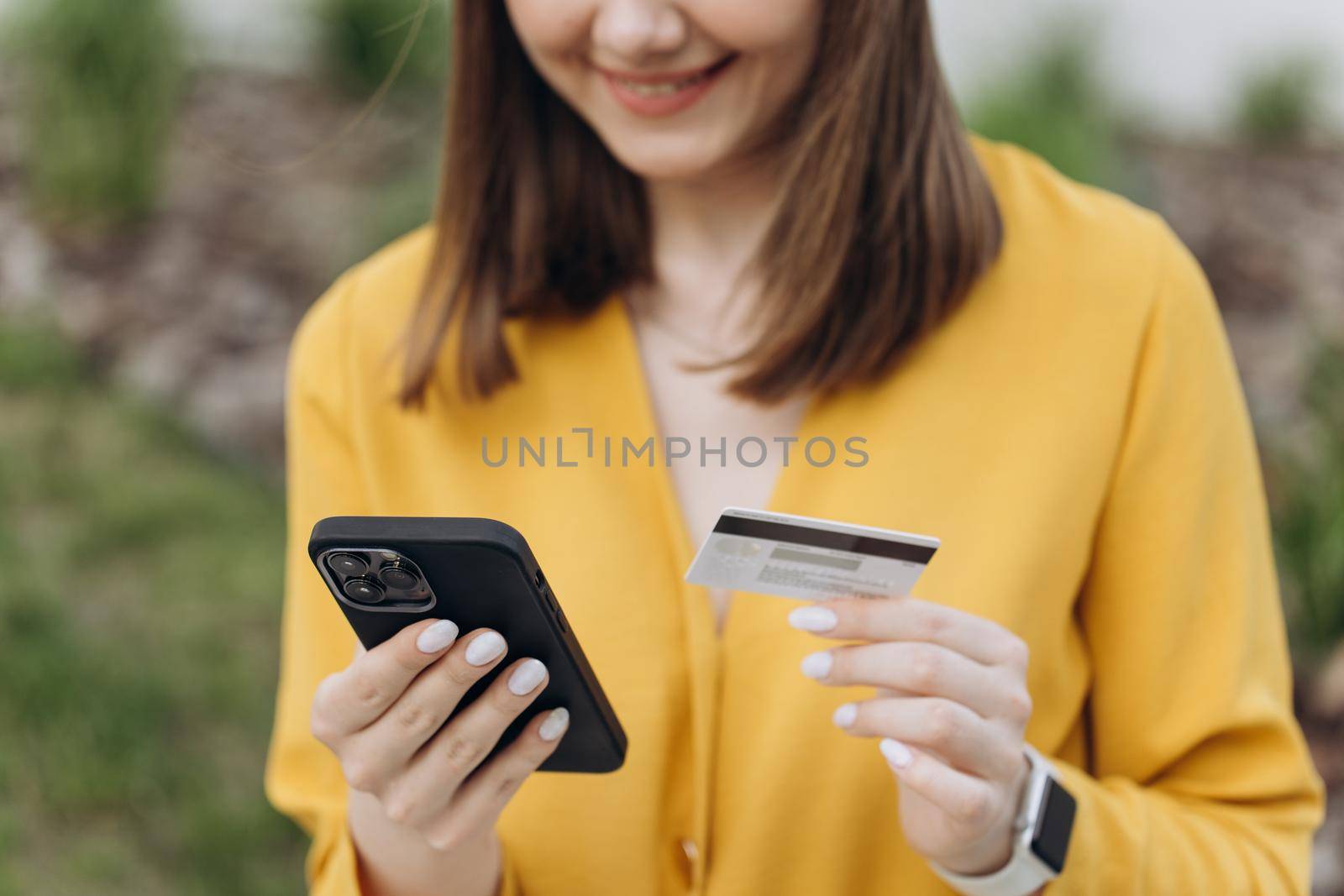 Close up female hands holding credit card and smartphone. Young woman paying online, using banking service, entering information, shopping, ordering in internet store, doing secure payment