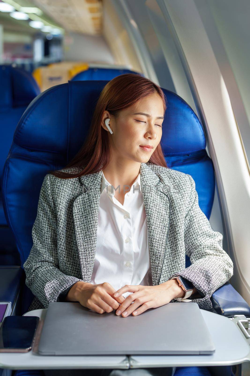 portrait of Successful Asian businesswoman or entrepreneur in a formal suit on an airplane seated in business class. resting during the flight by Manastrong