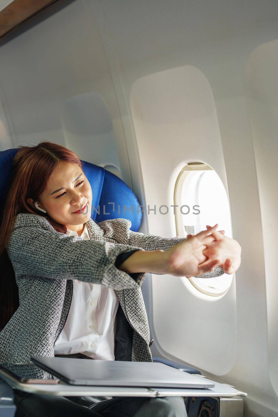 Portrait of a successful Asian businesswoman or entrepreneur in a formal suit on an airplane in business class waking up from resting between flights.