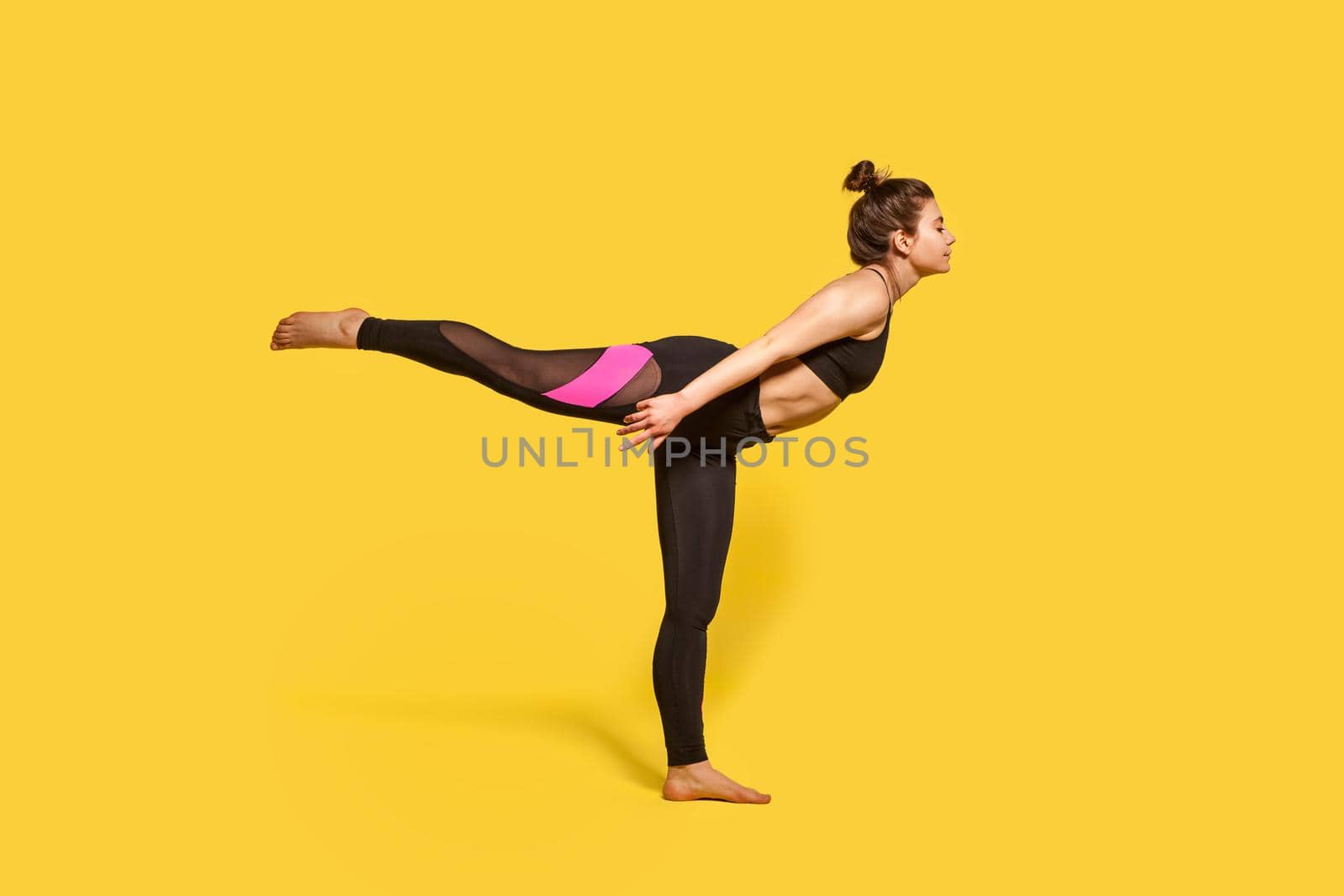 Warrior 3 pose. Slim woman with hair bun in tight sportswear practicing yoga, doing Virabhadrasana III exercise on one leg, stretching muscles and balancing. studio shot, sport workouts isolated