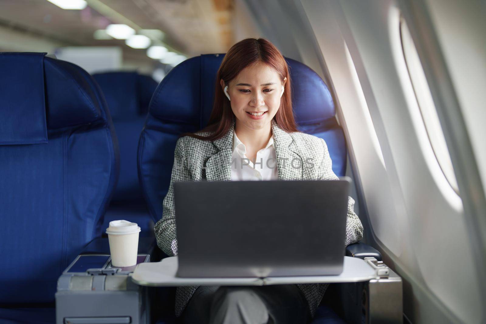 portrait of A successful asian businesswoman or female entrepreneur in formal suit in a plane sits in a business class seat and uses a computer laptop during flight.