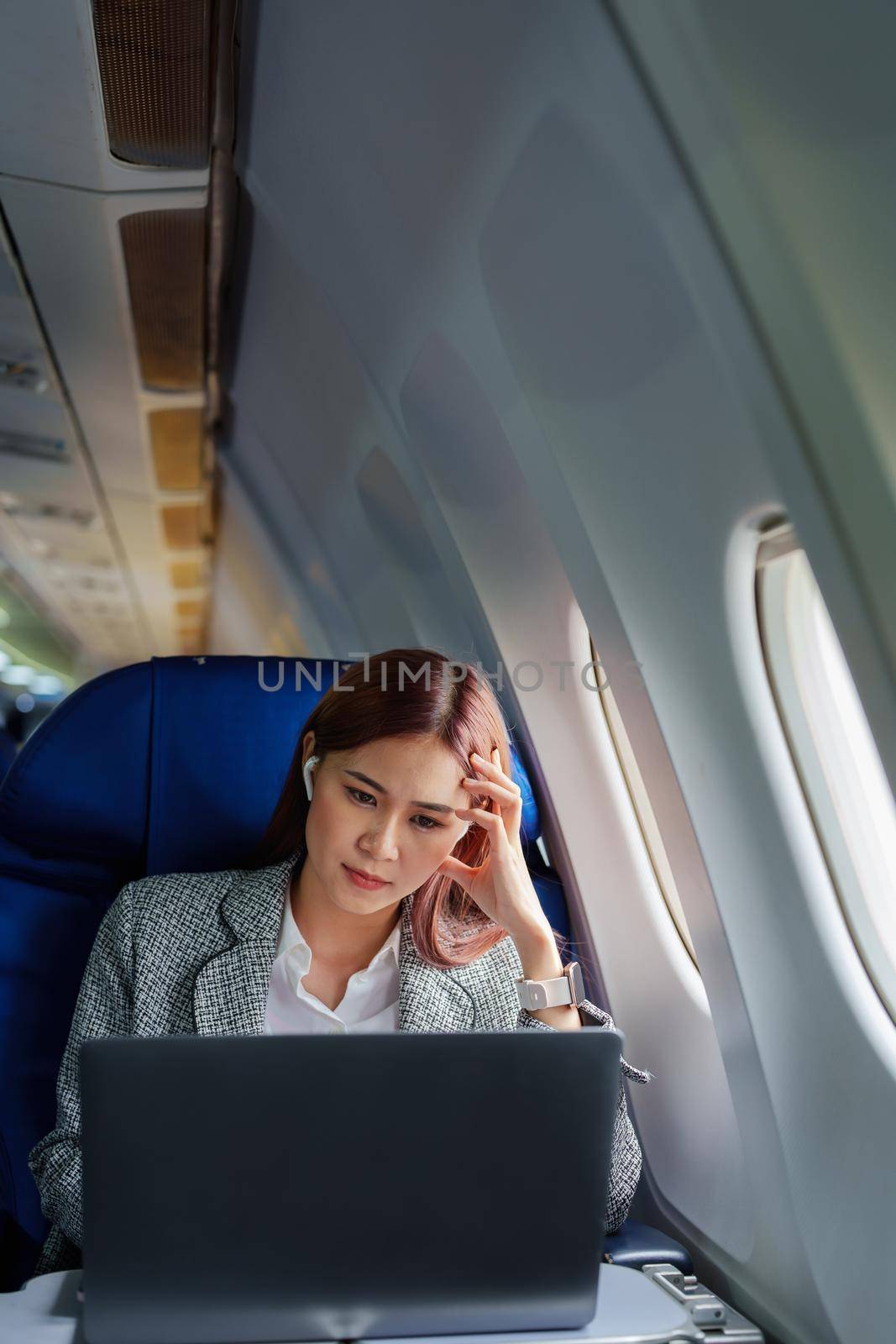 portrait of A successful asian businesswoman or female entrepreneur in formal suit in a plane sits in a business class seat and uses a computer laptop during flight by Manastrong