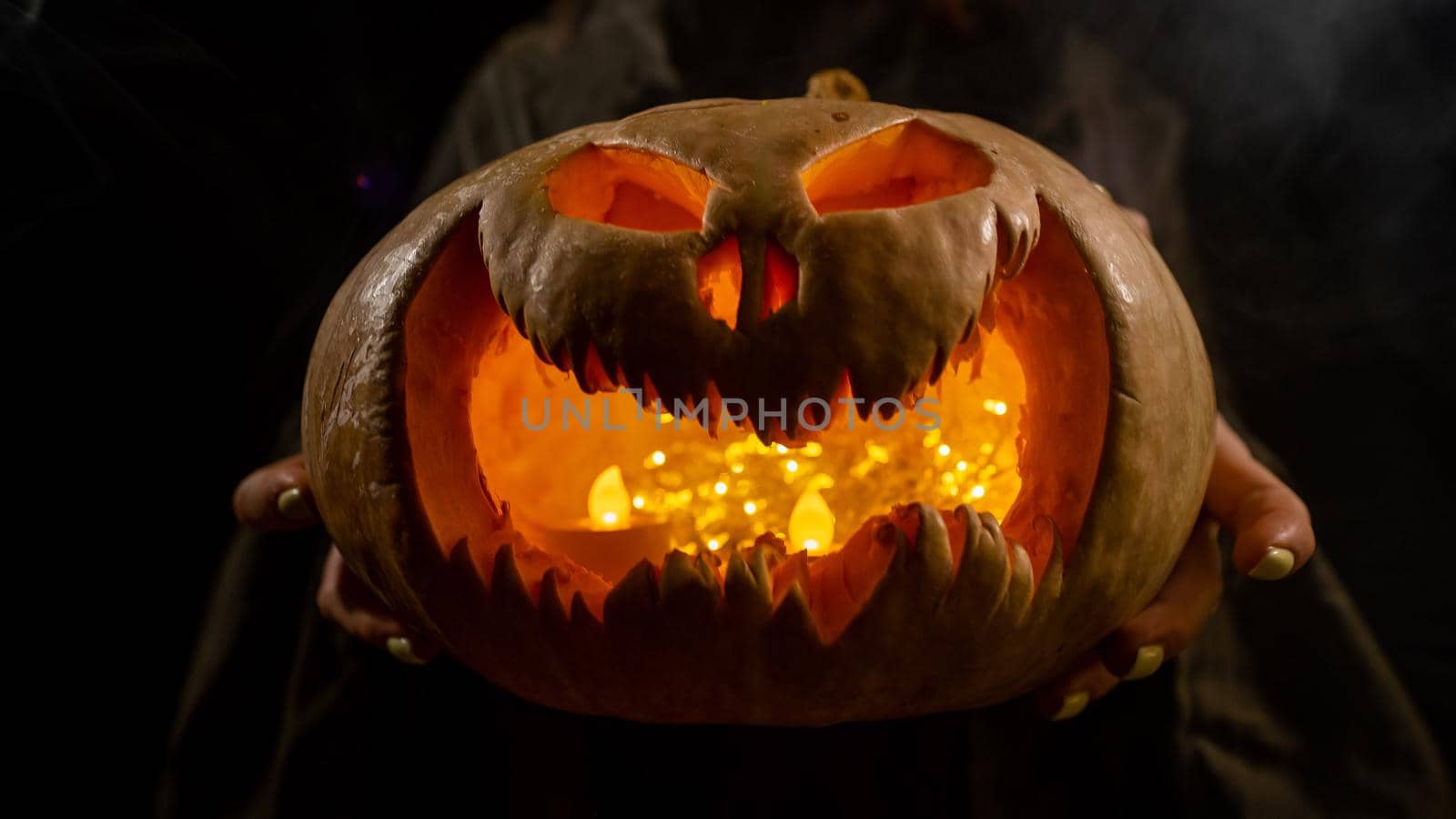 The witch is holding a pumpkin jack about a lantern glowing in the dark. Halloween