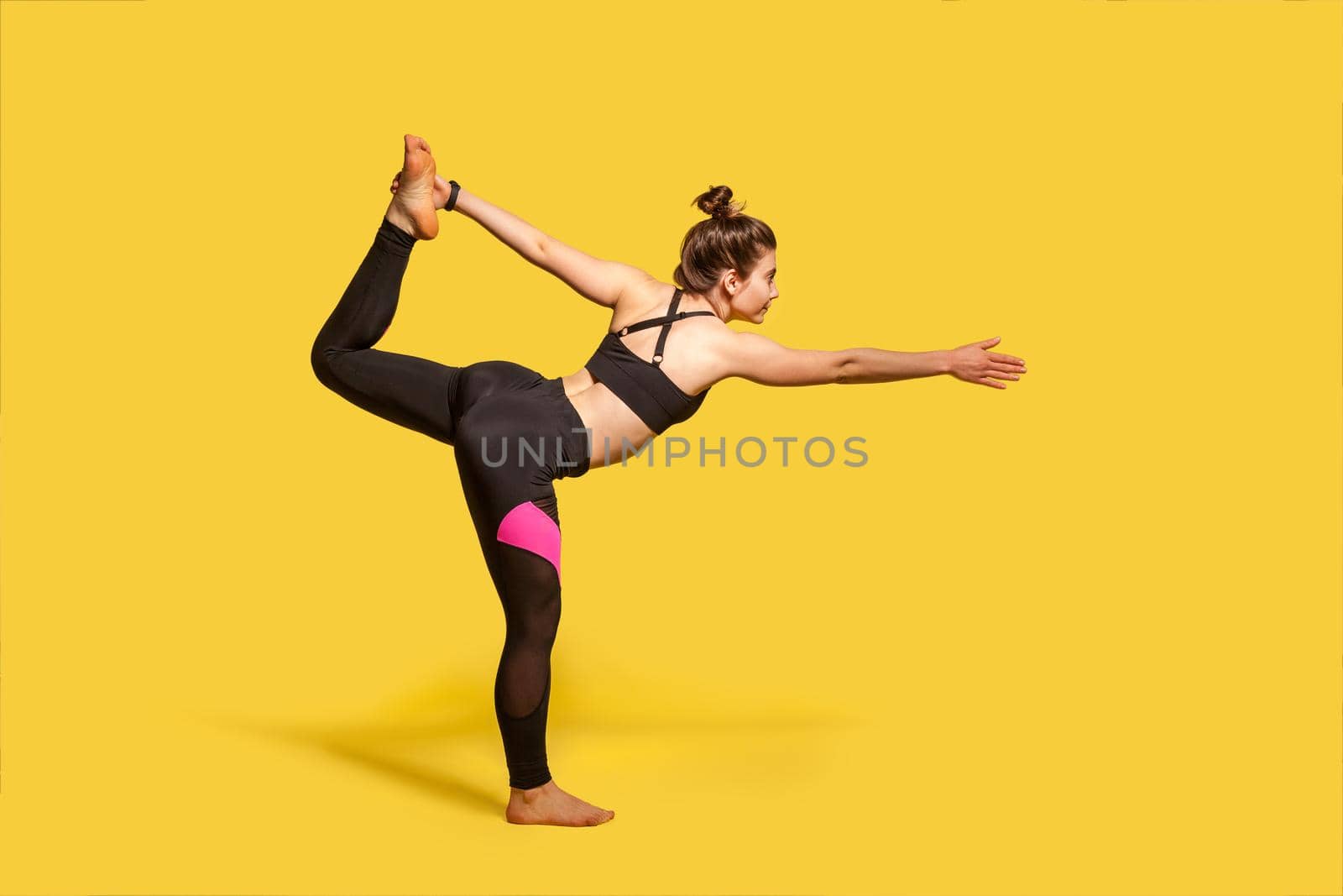 Dancer pose. Slim woman with hair bun in tight sportswear practicing yoga, doing Natarajasana exercise on one leg, stretching muscles and balancing. full length studio shot, sport workouts isolated