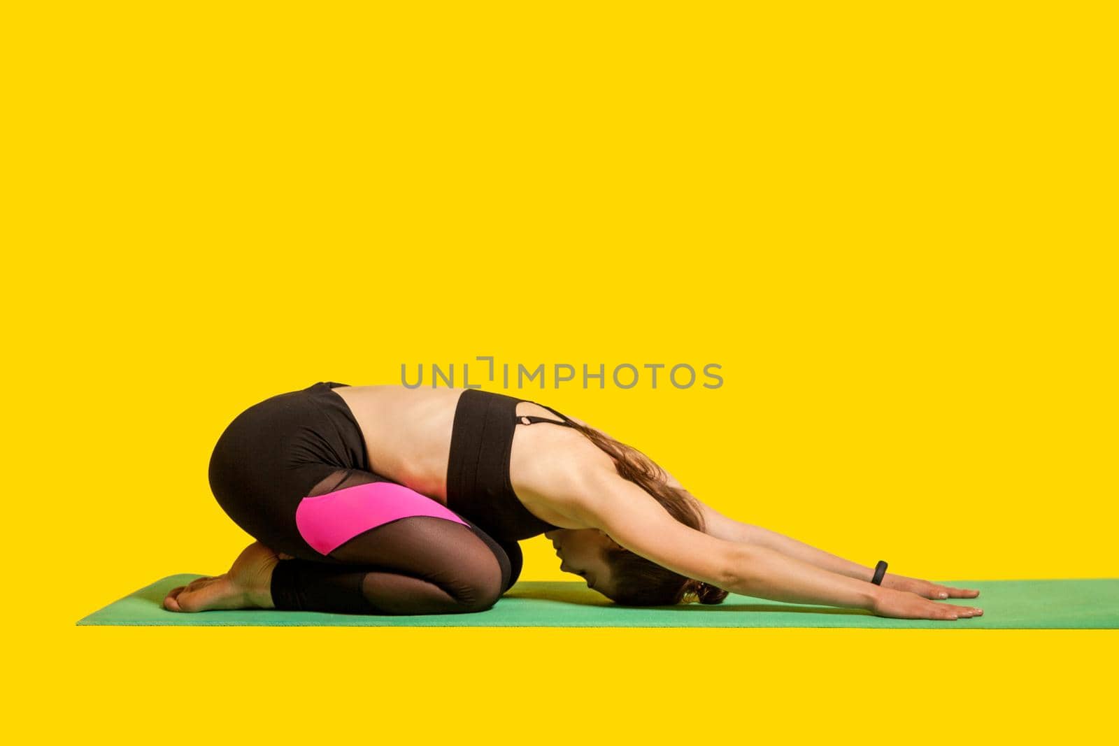 Child's pose. Young fit woman practicing yoga, doing seated forward bend Balasana exercise, stretching hands and back muscles for better flexibility. indoor studio shot, sport workouts isolated