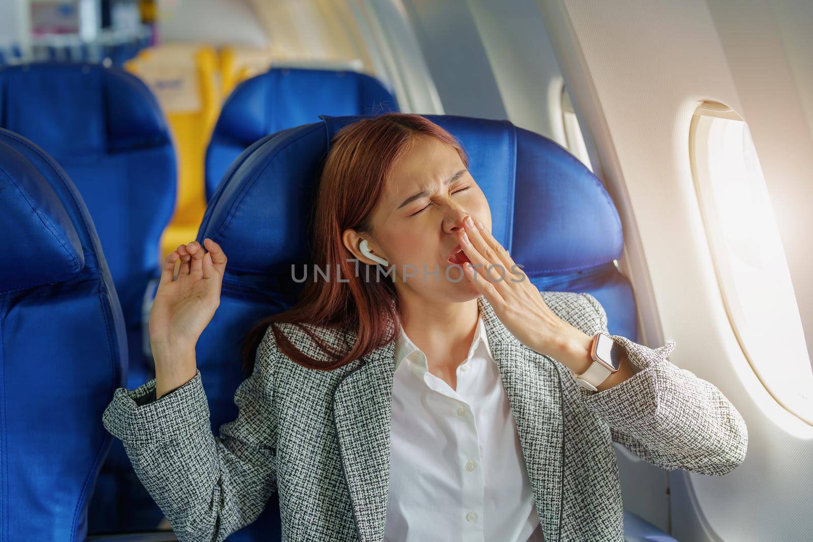 Portrait of a successful Asian businesswoman or entrepreneur in a formal suit on an airplane in business class waking up from resting between flights.