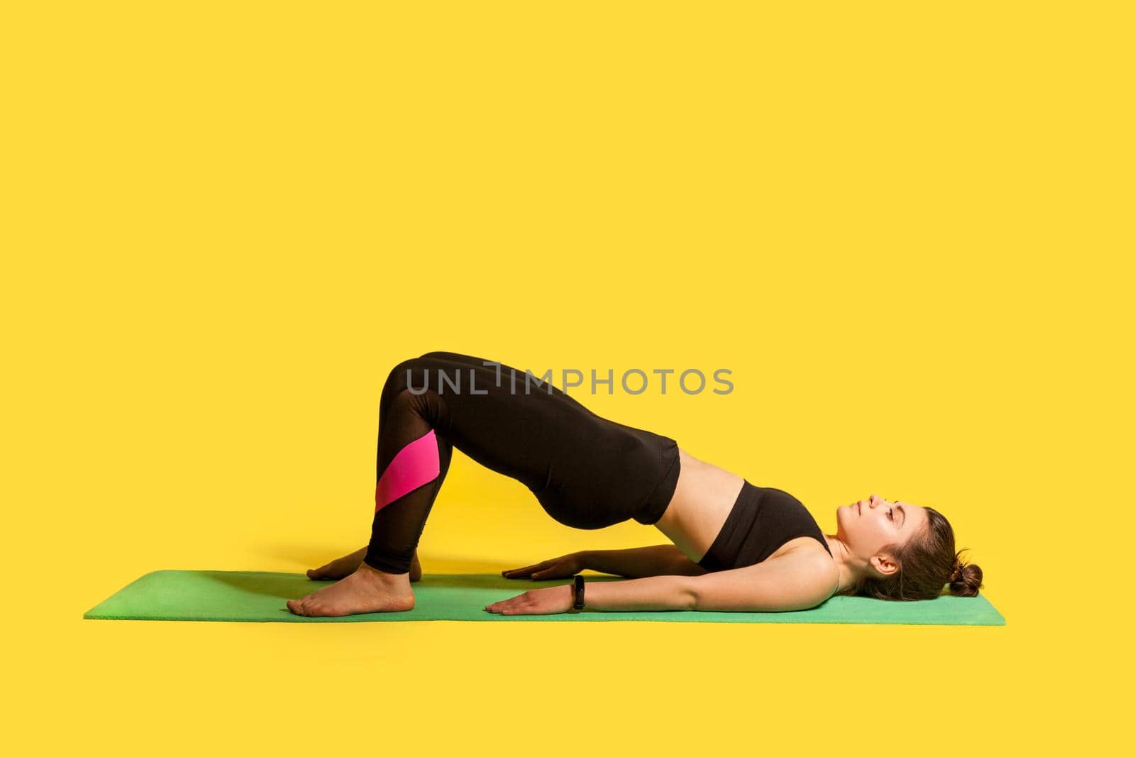 Bridge pose. Young fitness woman in tight sportswear practicing yoga, bending back, stretching spinal muscles, doing flexibility exercises. studio shot, sport workouts isolated on yellow background