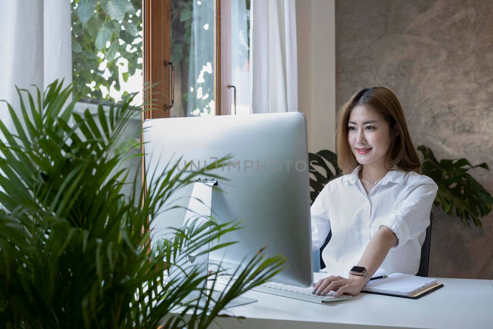Happy young woman entrepreneur working with computer at comfortable workplace. by prathanchorruangsak