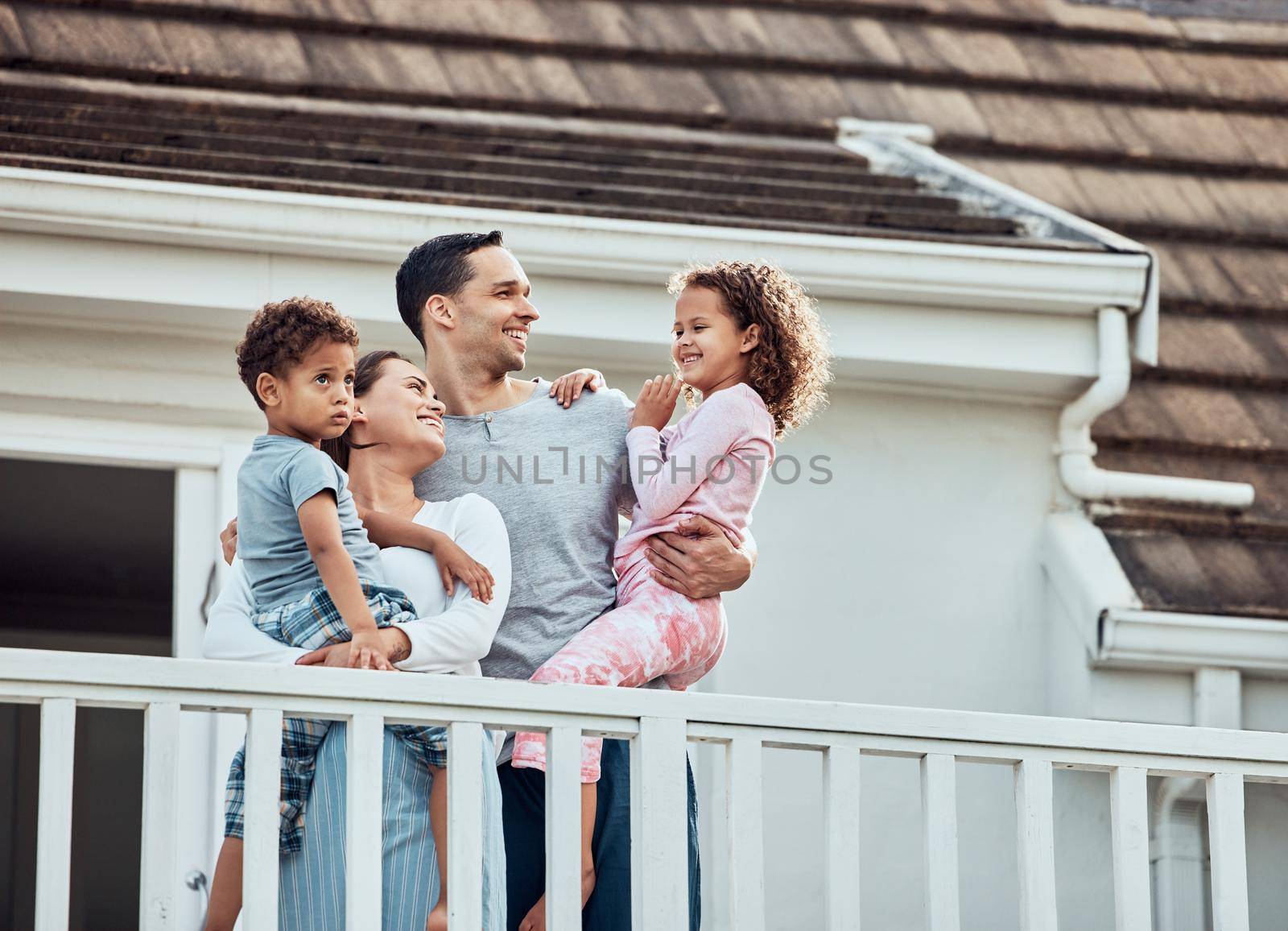 Happy young mixed race family with two children standing outside on their balcony at home. Loving couple with their daughter and son wearing pyjamas and enjoying their new house.