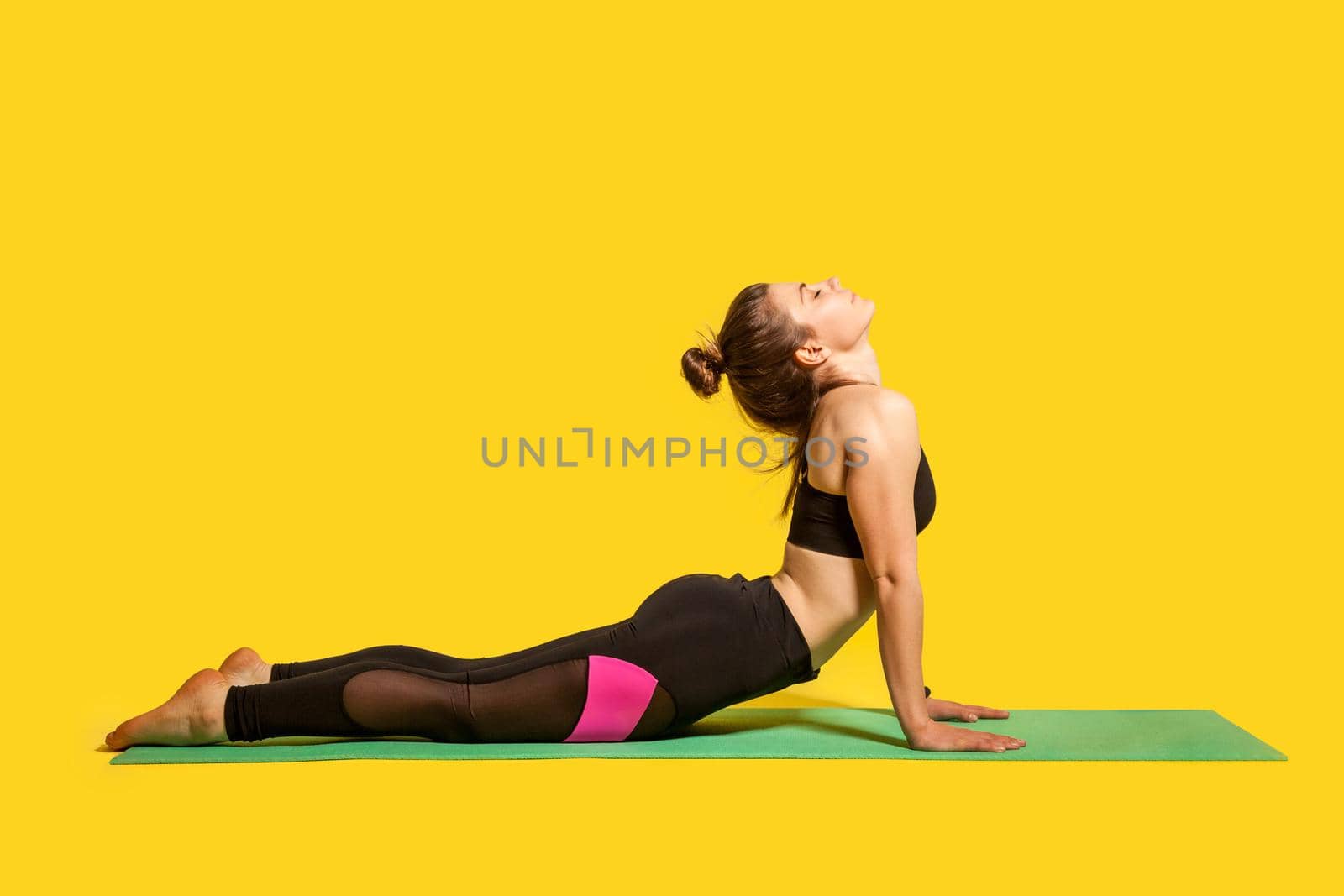 Cobra pose. Young fit woman in tight sportswear practicing yoga, doing bhujangasana exercise on hands, stretching back muscles for better flexibility. indoor studio shot, sport workouts isolated