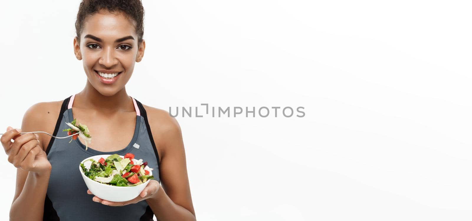 Healthy and Fitness concept - Beautiful American African lady in fitness clothes on diet eating fresh salad. Isolated on white background