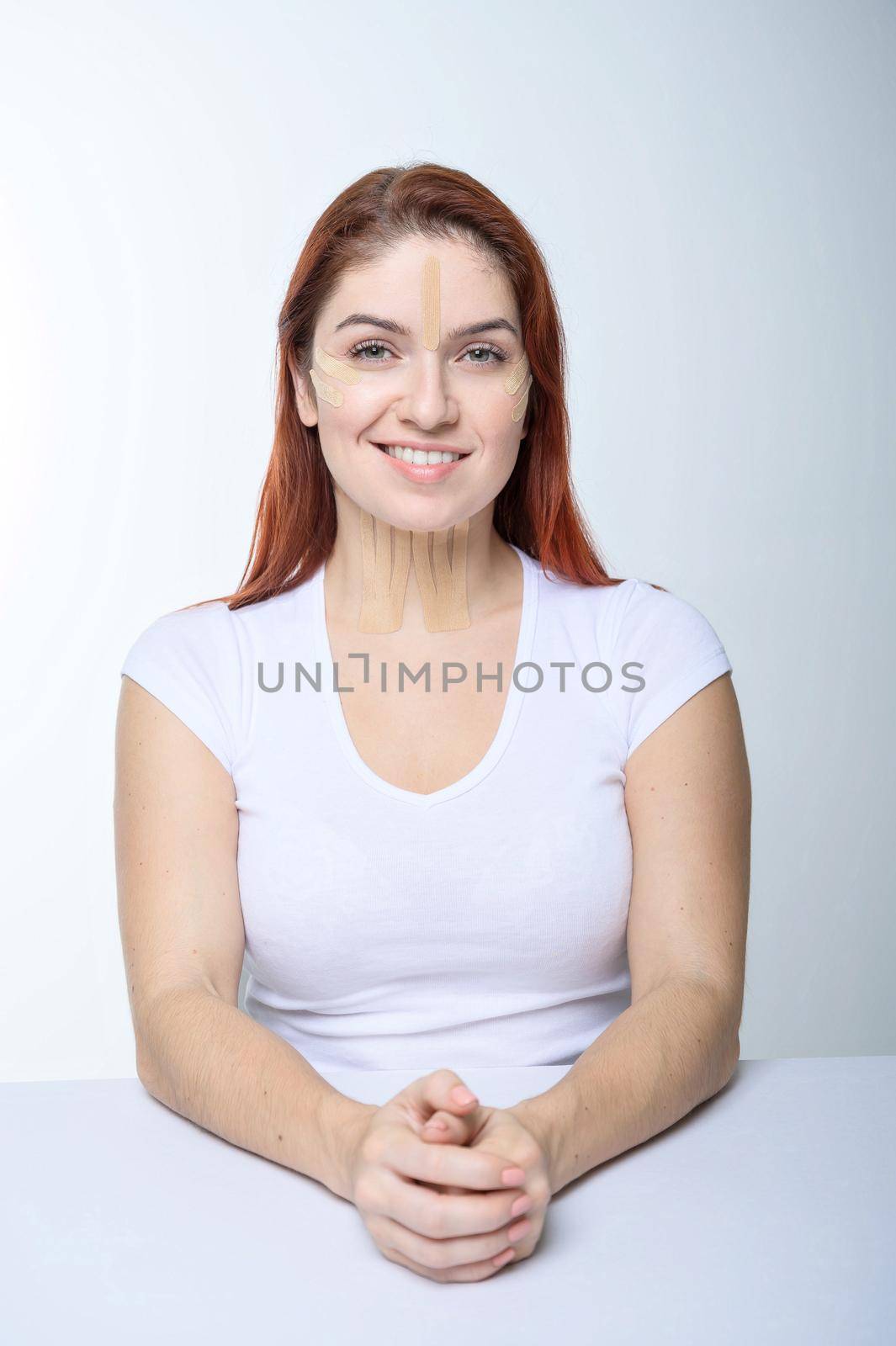 Portrait of a redhead woman with tapes on skin color face for rejuvenation. An alternative way to fight wrinkles