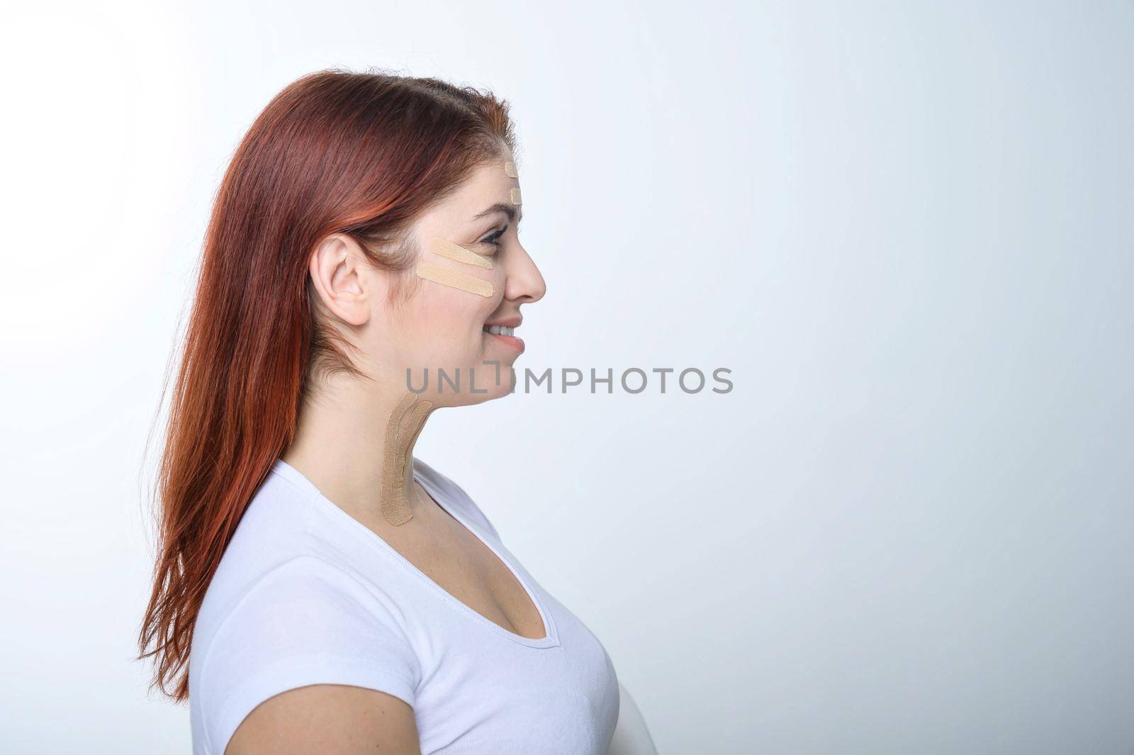 Profile red-haired woman with tape on the skin complexion rejuvenation. An alternative way to fight wrinkles