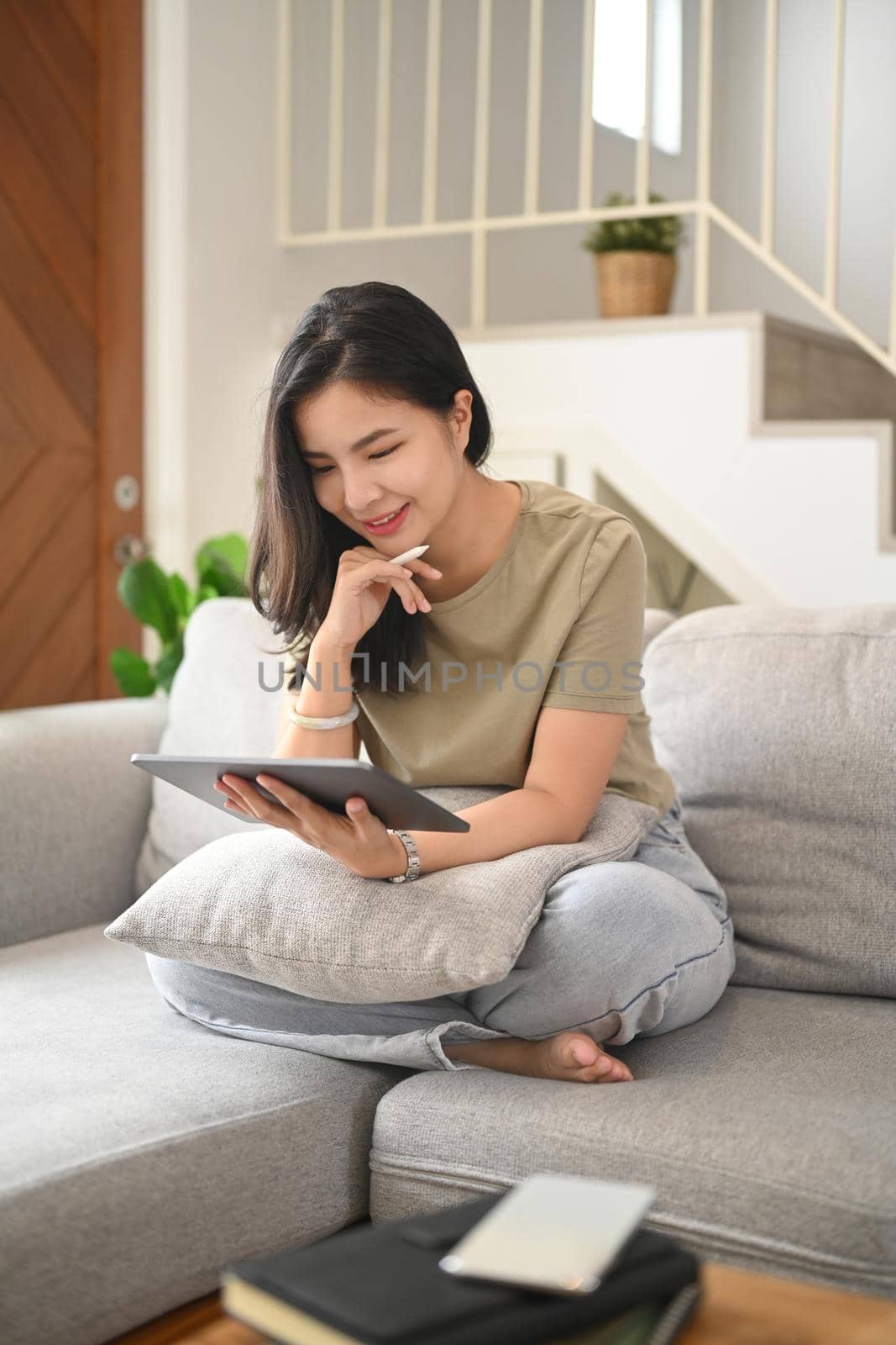 Smiling young woman resting on couch and browsing wireless internet on digital tablet. People, technology concept.