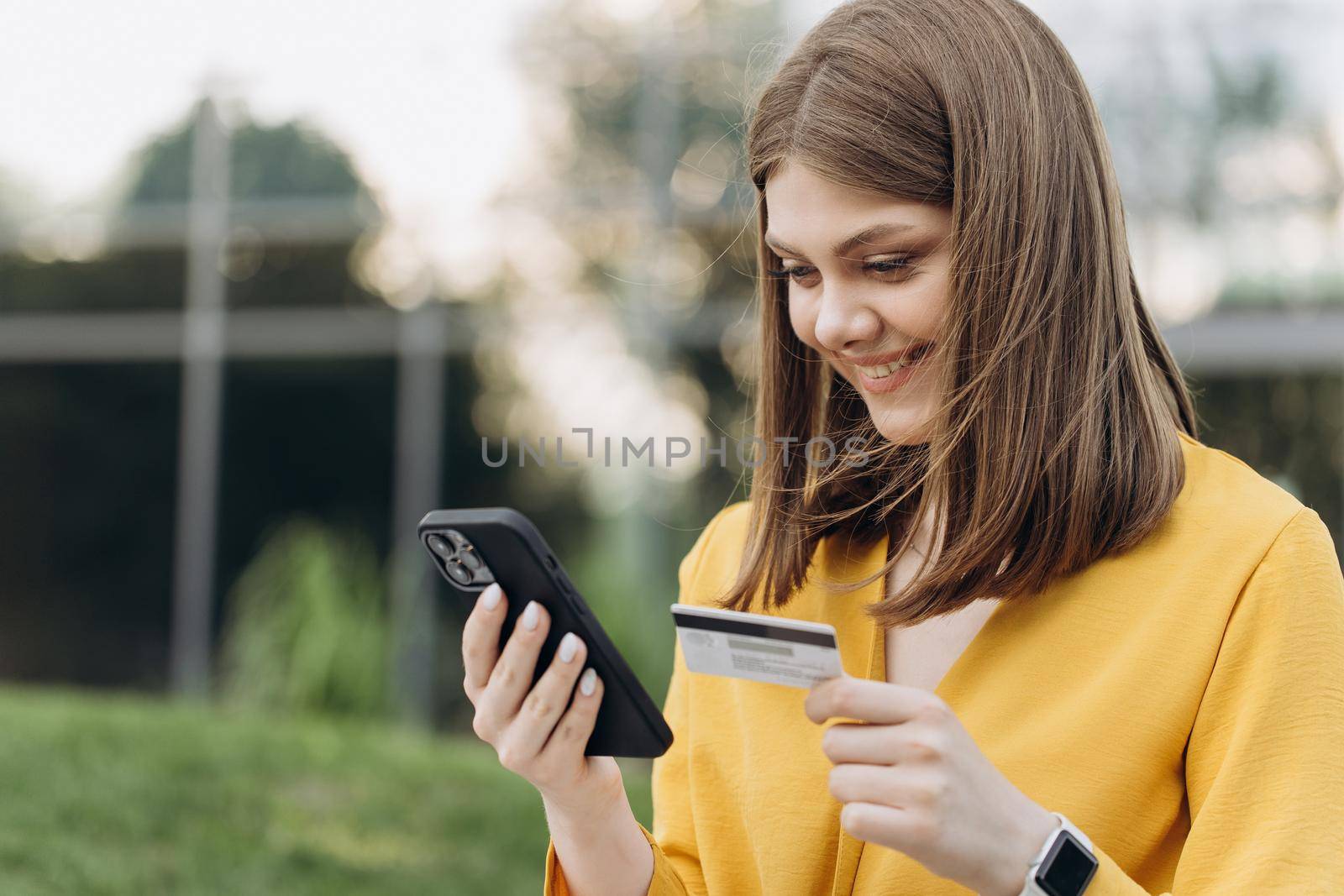 Happy caucasian woman buying things online using smartphone and credit card enjoying shopping in internet. Positive young girl purchasing goods on web, making remote payment. by uflypro