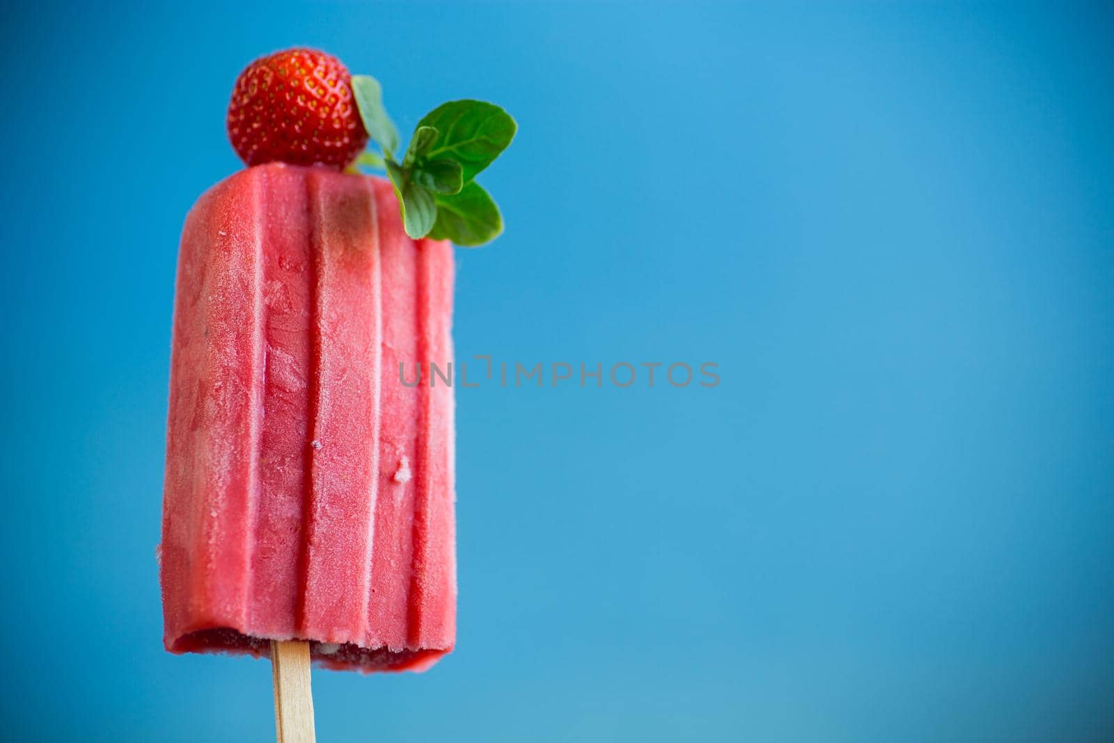 cooked homemade strawberry ice cream on a stick, isolated on blue background