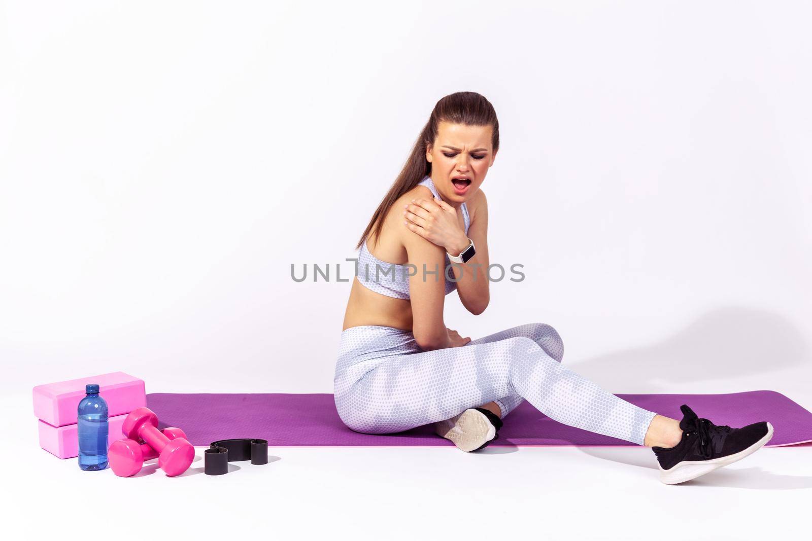 Full length athletic woman screaming feeling pain in shoulder, massaging sore spine, suffering back ache after exhausted exercising. Indoor studio shot isolated on gray background