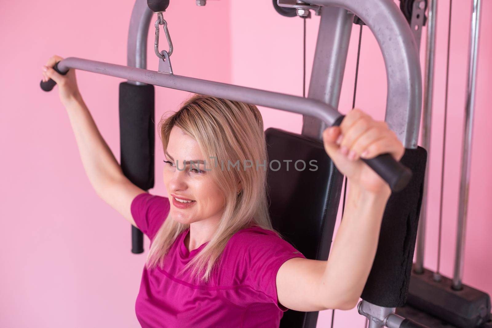 woman wearing pink and black professional sportswear pulling up at the gym. Strength and motivation concept. by Andelov13