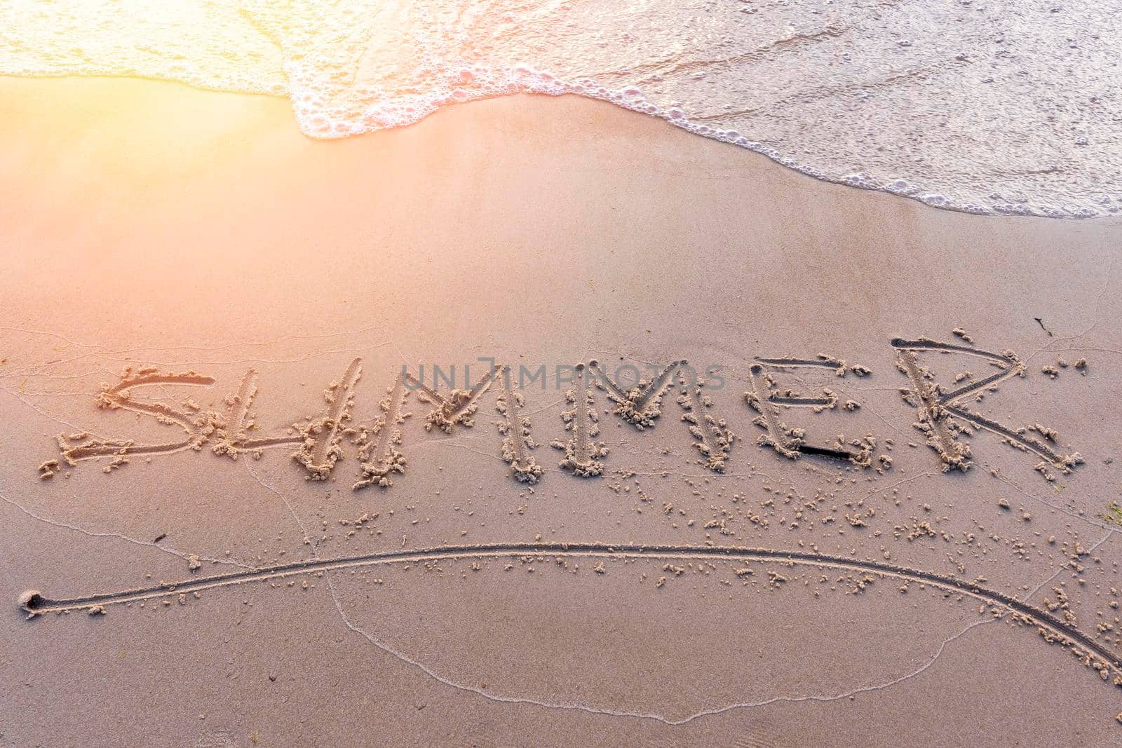 light waves of surf roll over the inscription the word Summer. the word Summer on the sand in the sunset light.