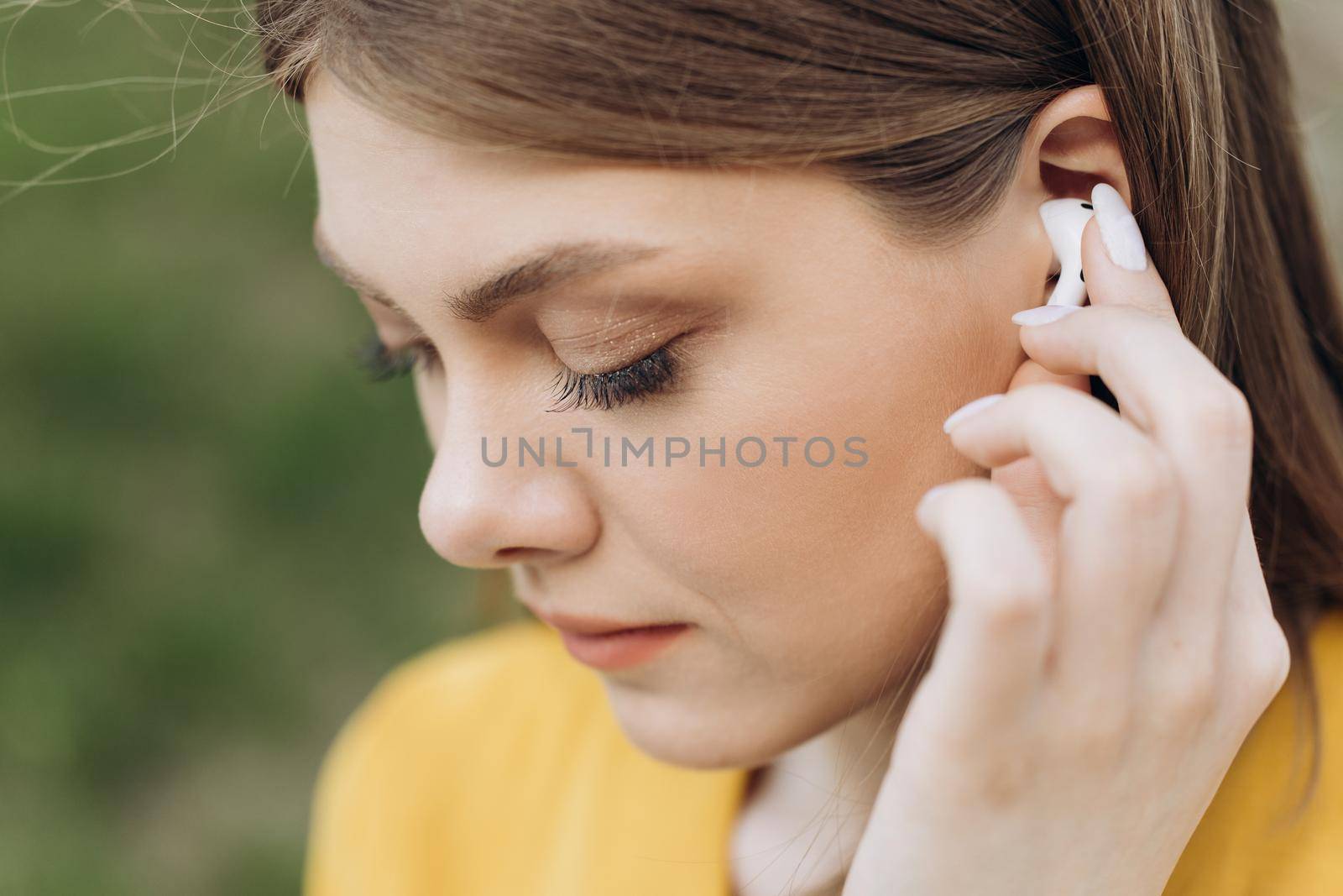 Young beautiful woman with wireless earphones on her ears. Close up of female ear with wireless earphone inside listening to music.