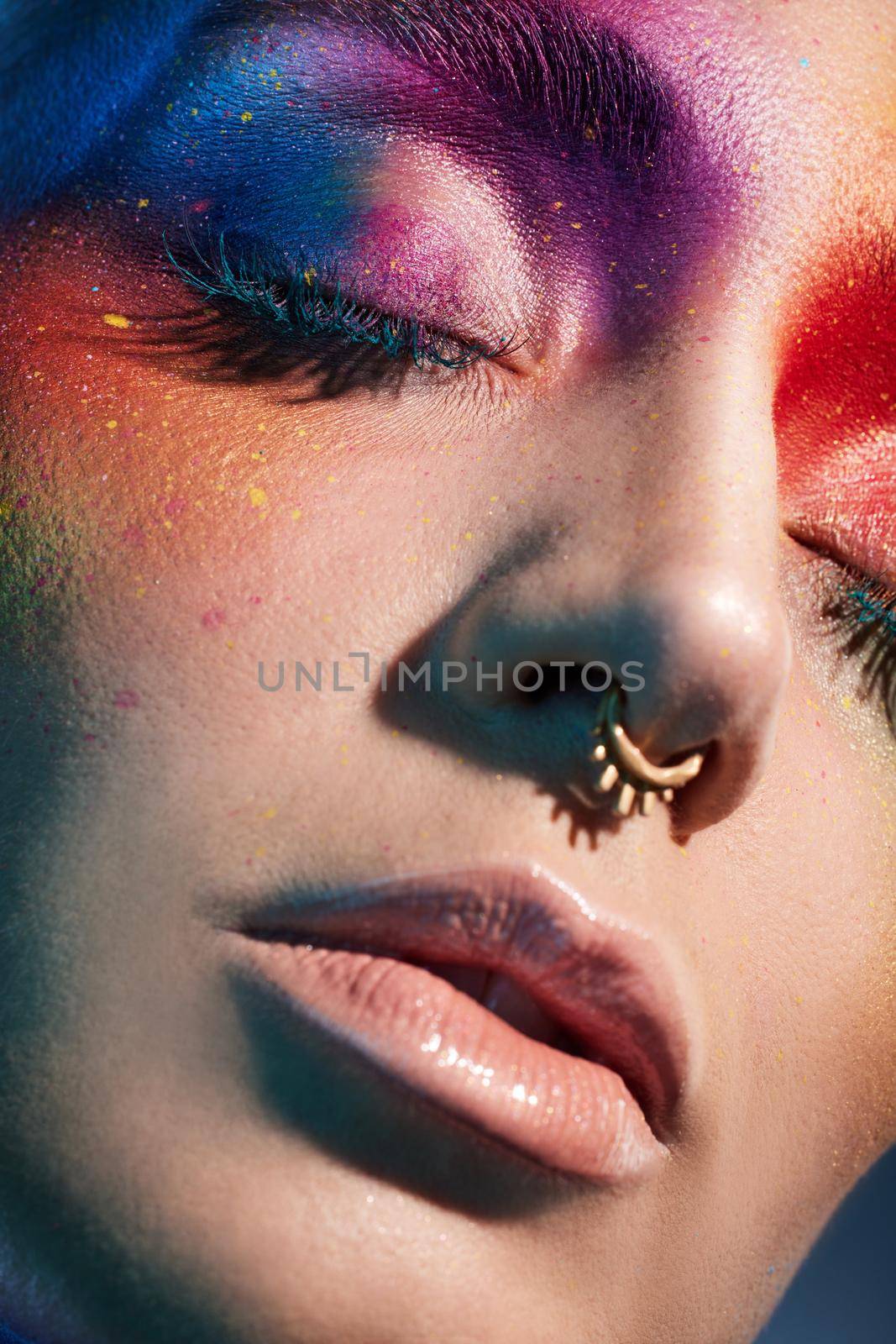 Studio shot of a young woman posing with multi-coloured paint on her face.